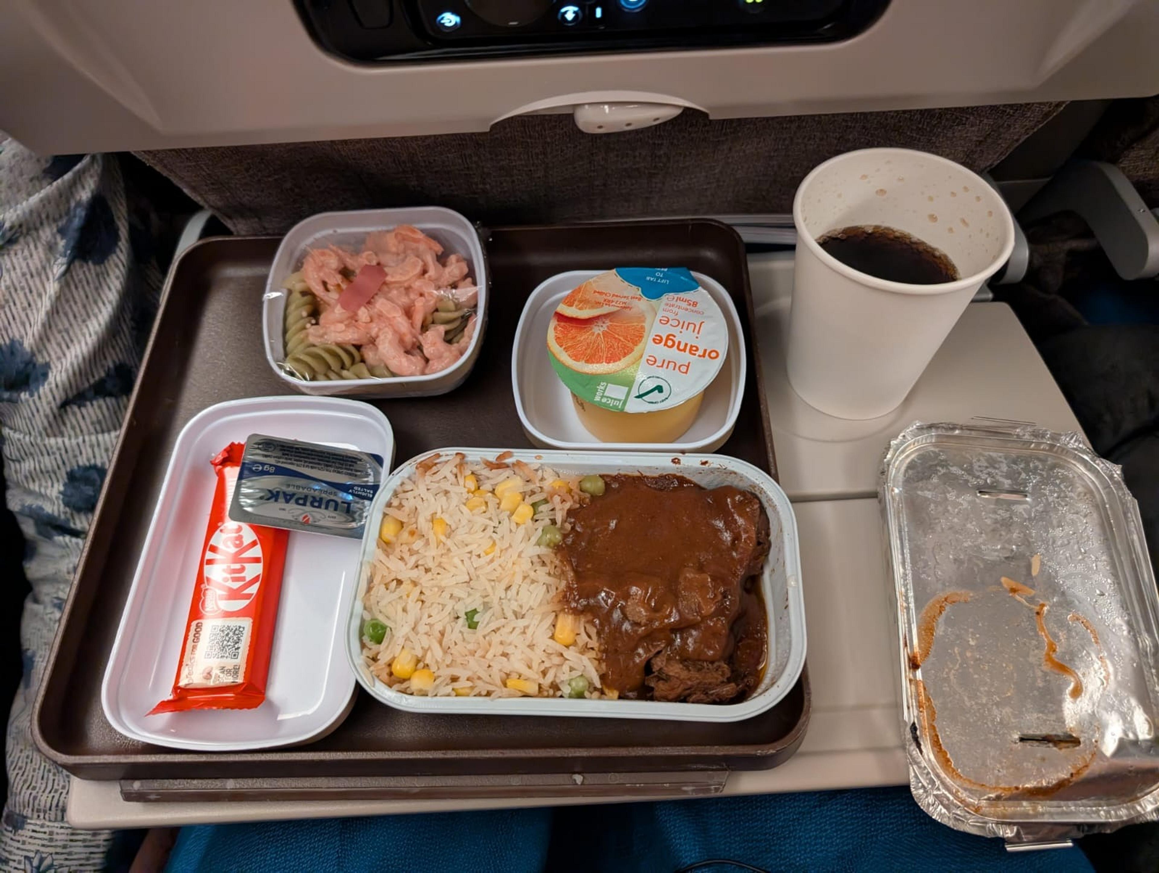 A China Eastern Airlines meal tray features beef with rice and vegetables, pasta salad, a Kit Kat bar, orange juice, and coffee.