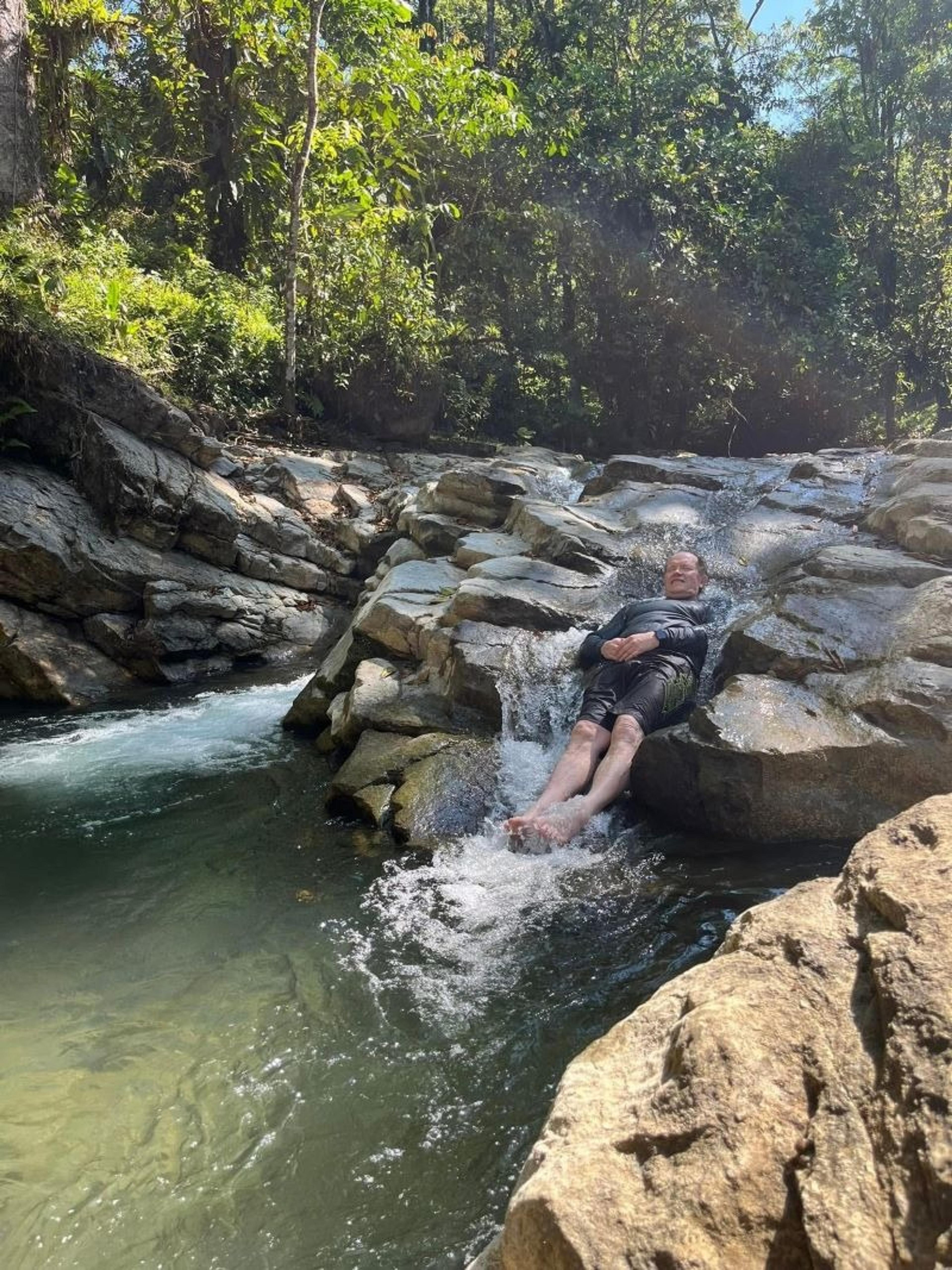 A person slides down a rocky stream within a lush forest in Costa Rica.
