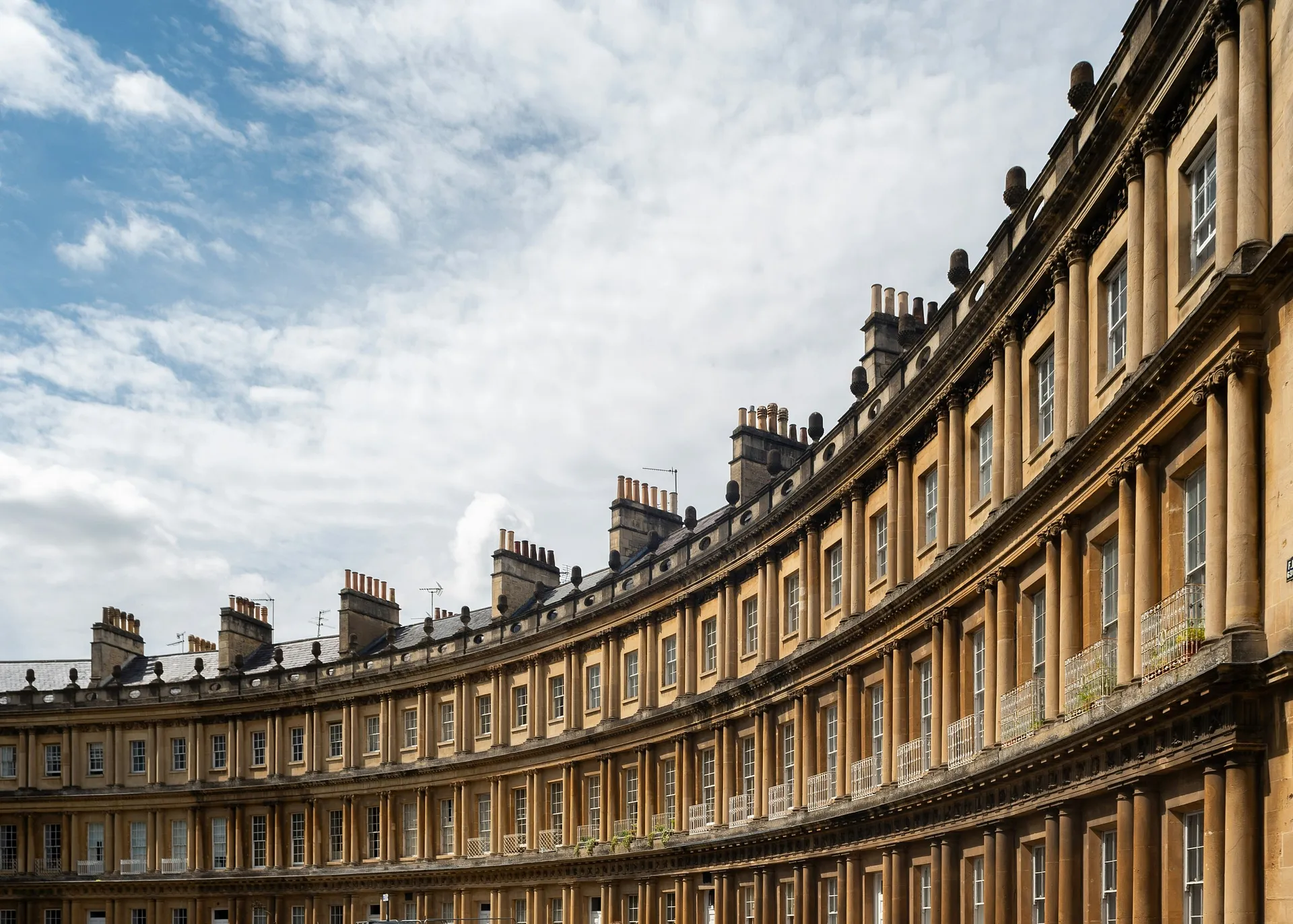 A sweeping curve of Georgian townhouses characterizes the architecture of The Circus in Bath, England, under a partly cloudy sky.