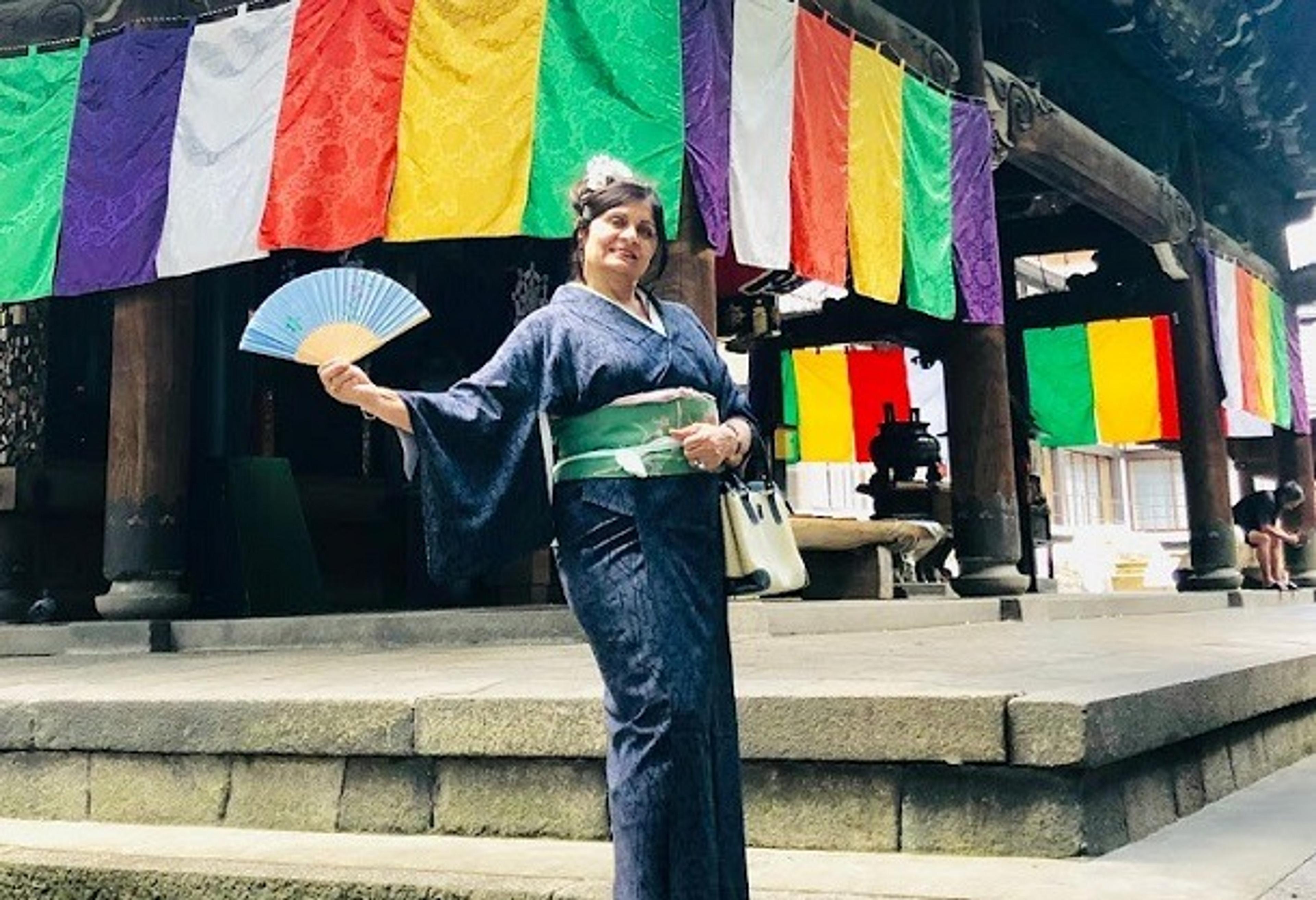 Priti, wearing traditional Japanese dress, stands in front of brightly coloured hanging fabrics