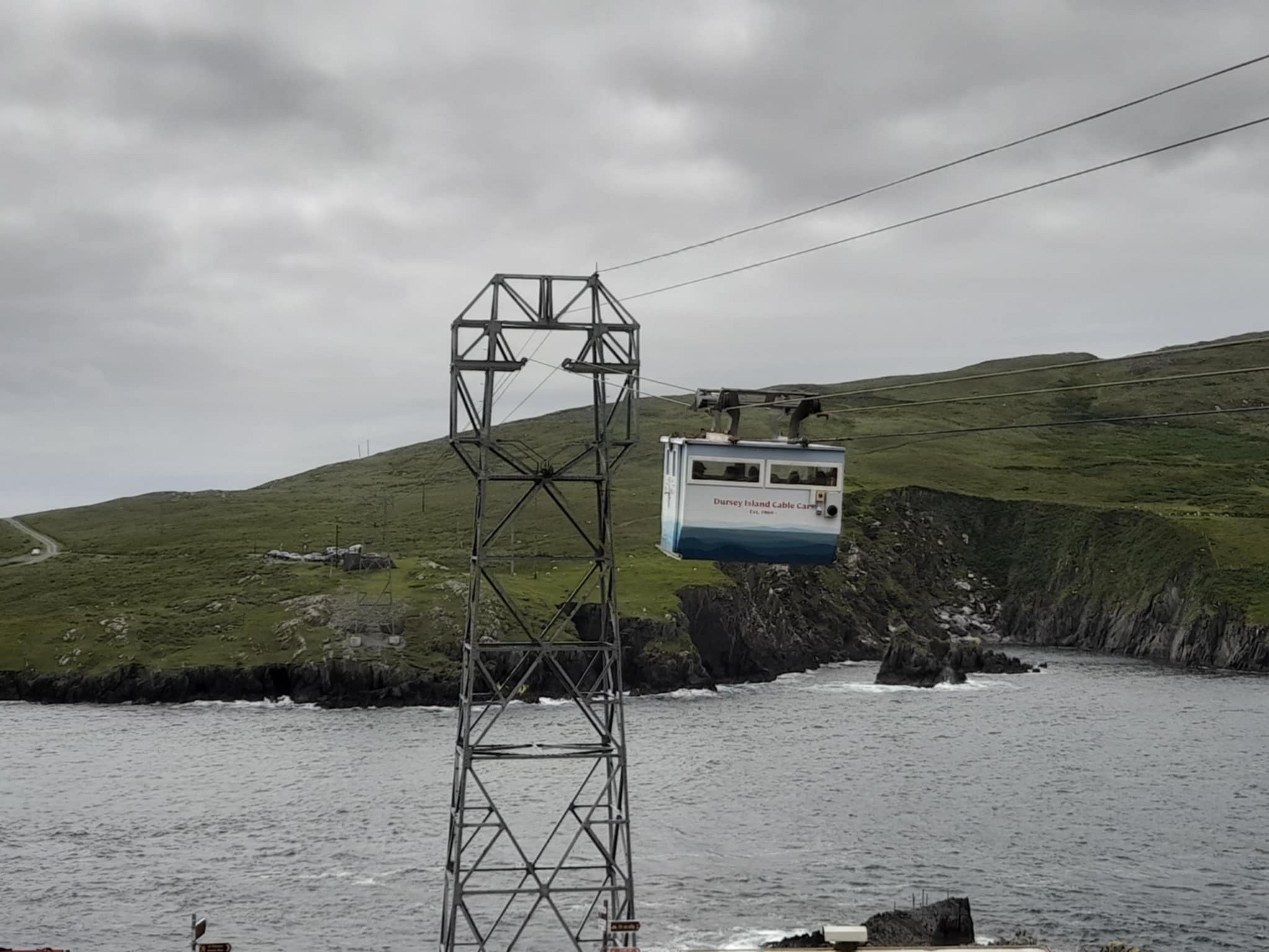 A cable car traverses over rugged cliffs and the sea at Dursey Island in Ireland.