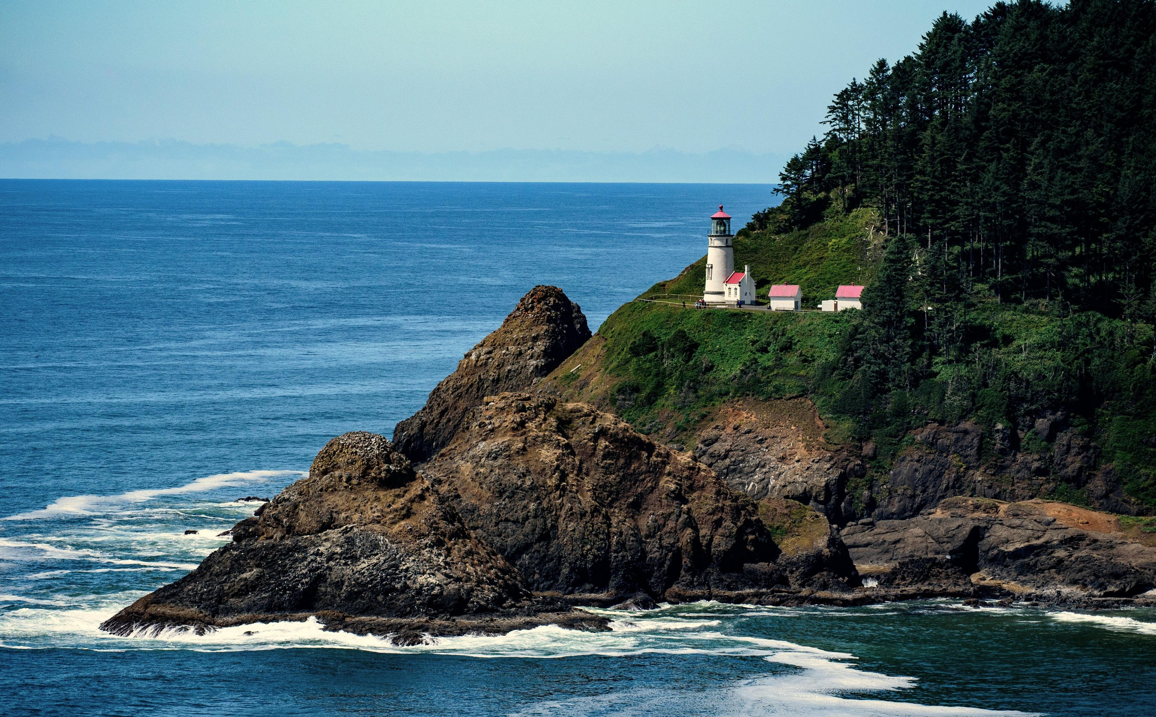 A lighthouse stands atop a rocky, forested cliff overlooking Cape Cove in Oregon.