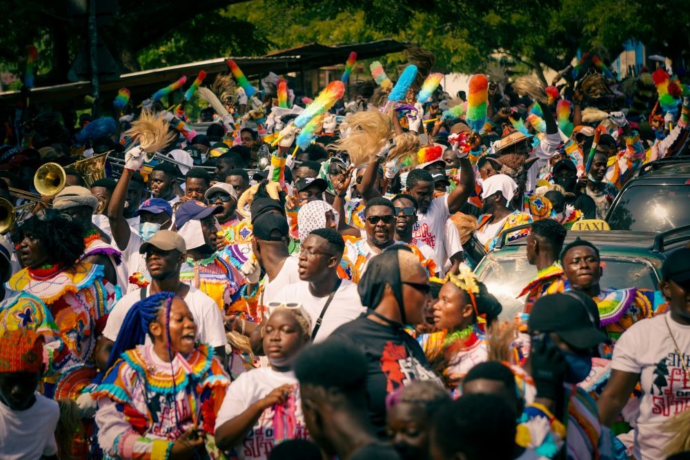 A vibrant street parade in Ghana features celebrants in colorful costumes with musical instruments and festive decorations.