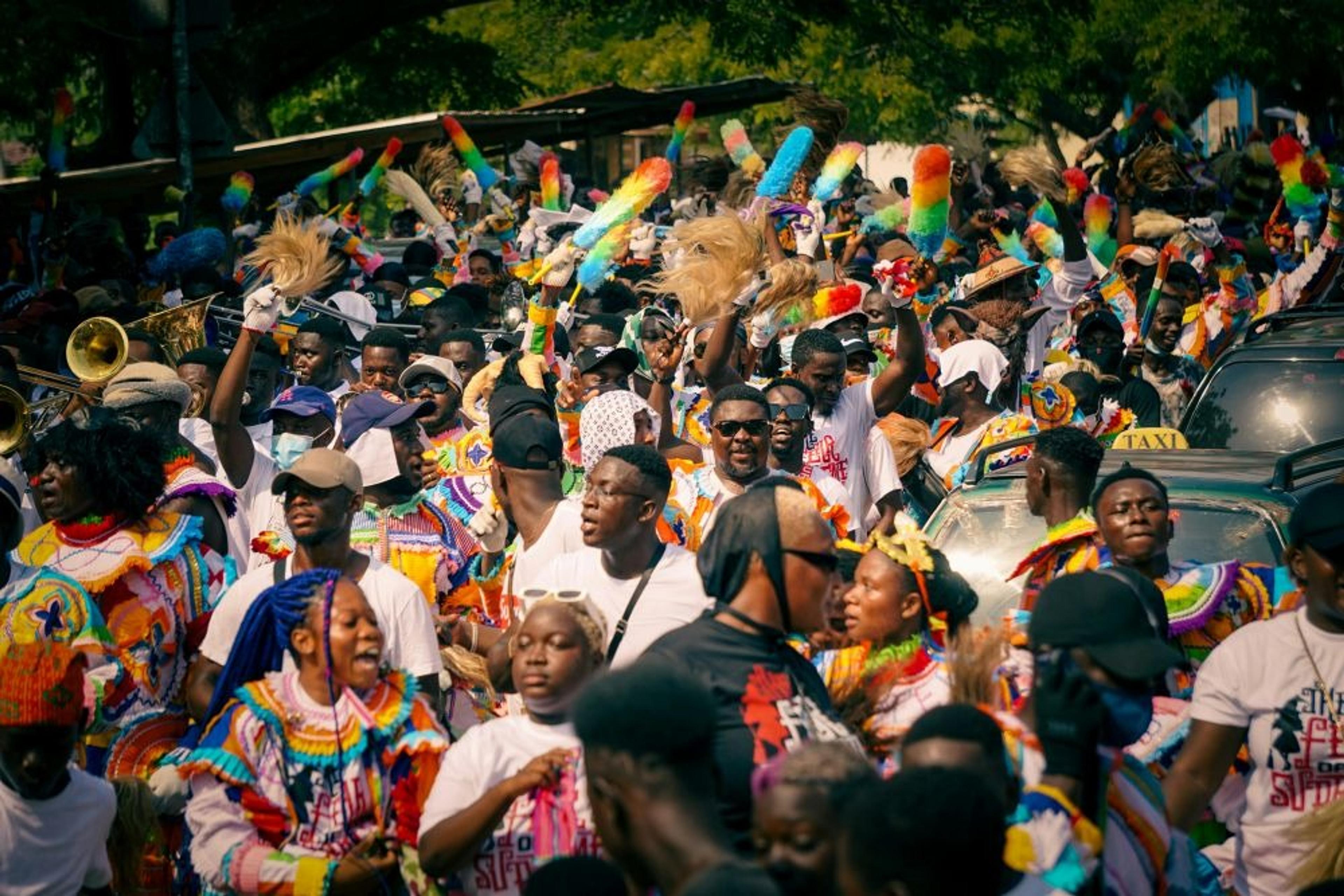 A vibrant street parade in Ghana features celebrants in colorful costumes with musical instruments and festive decorations.