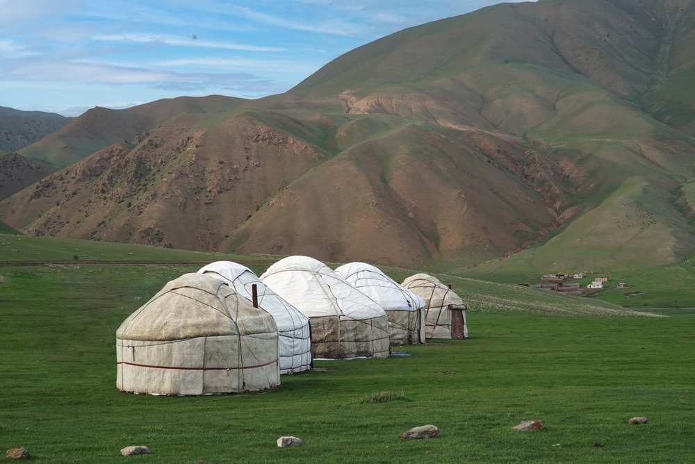 Yurts sit peacefully on the lush green steppe of Kyrgyzstan with rolling hills in the background.