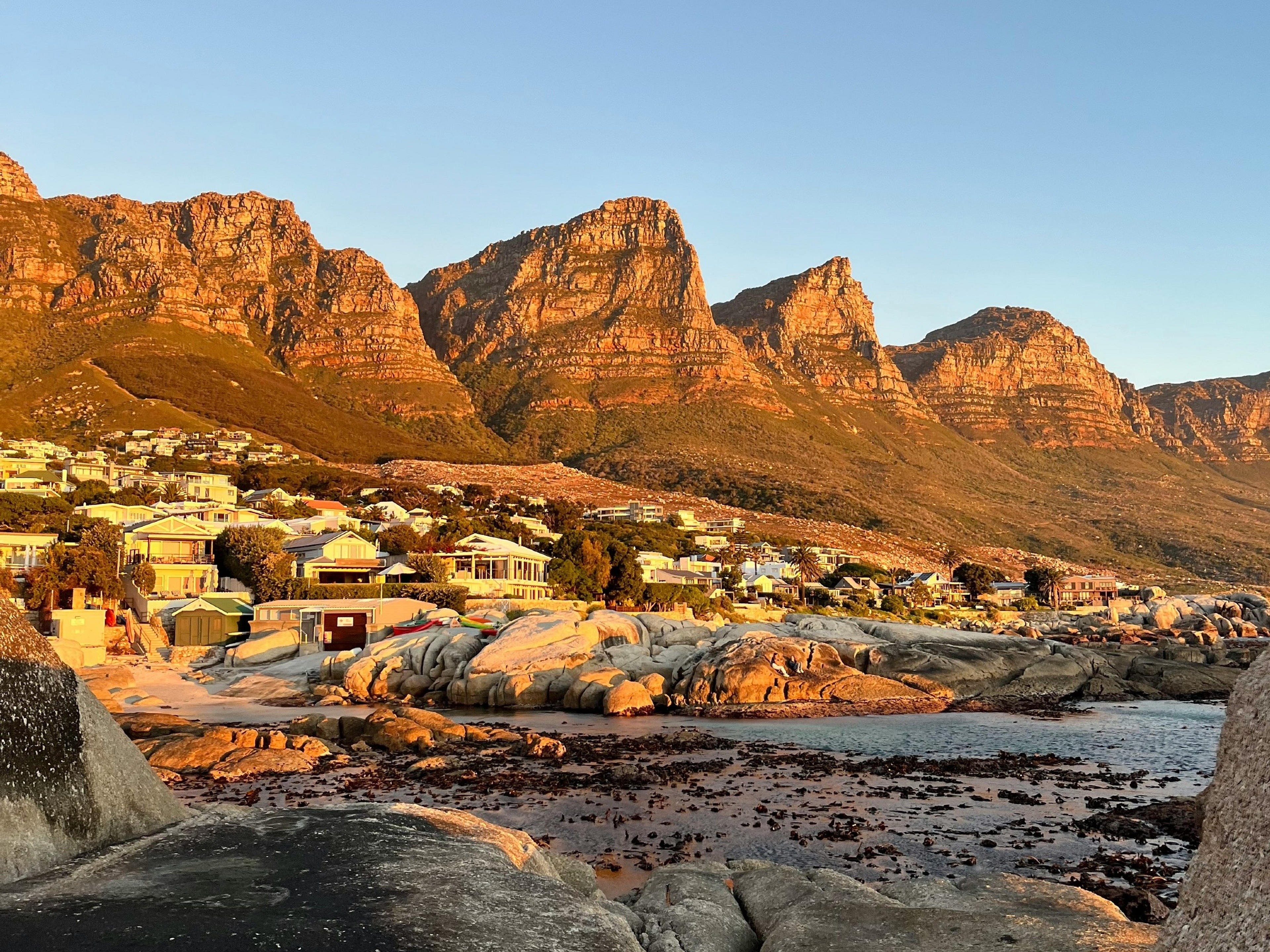 Golden light bathes the Twelve Apostles mountain range and the coastal houses of Cape Town.