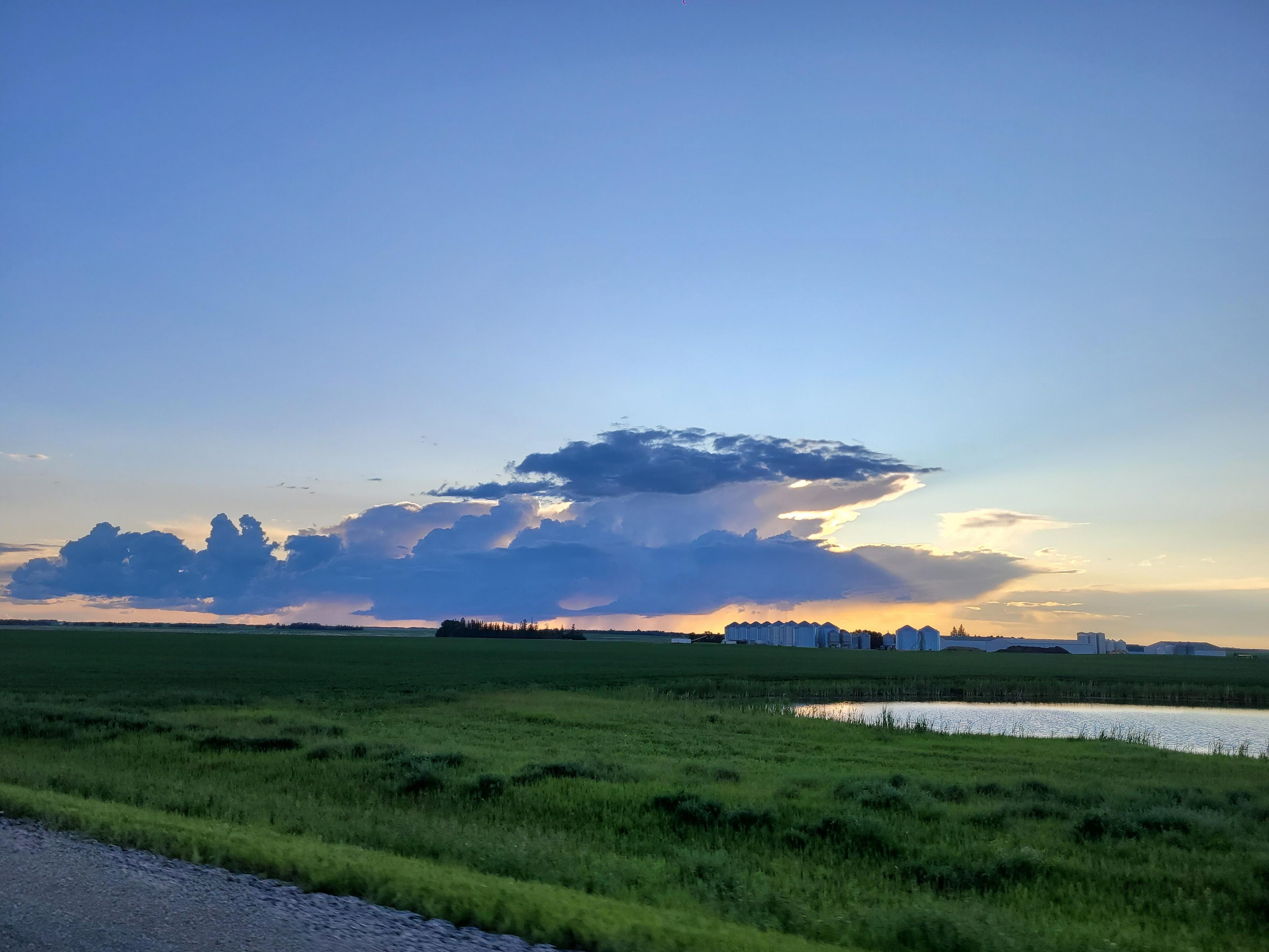 A stormy sunset sky stretches over the expansive prairies near Regina, Saskatchewan, with scattered silos dotting the horizon.