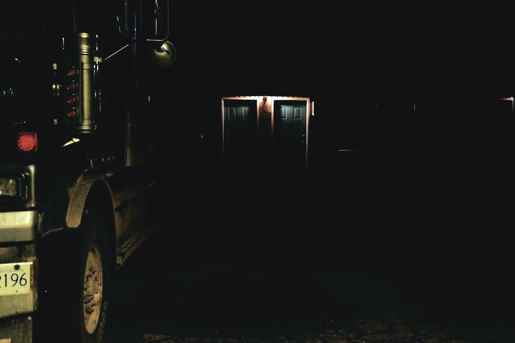 A motel door in the night illuminated by flickering light and a truck parked outside
