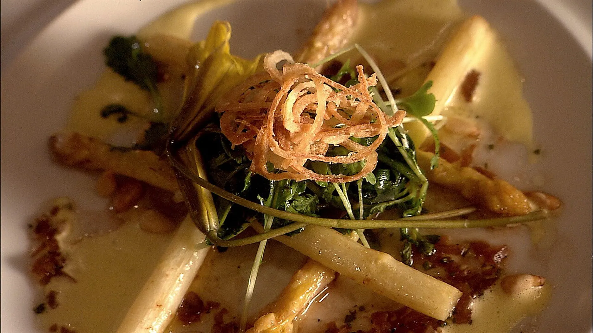 A gourmet dish featuring white asparagus and crispy onions artistically arranged on a plate.