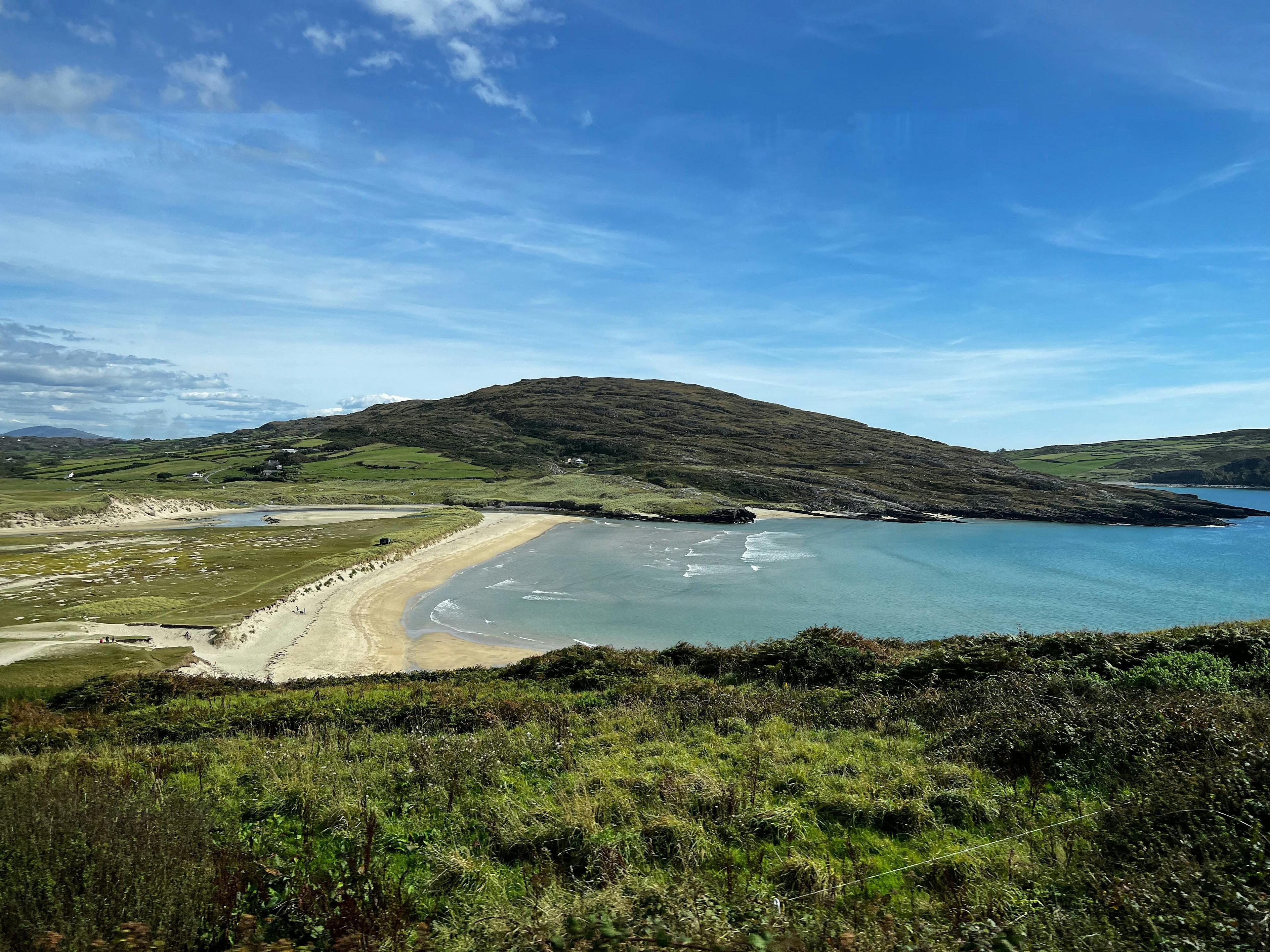 A serene coastal landscape featuring Barleycove Beach in West Cork, Ireland, is depicted with rolling green hills and a wide sandy shore.