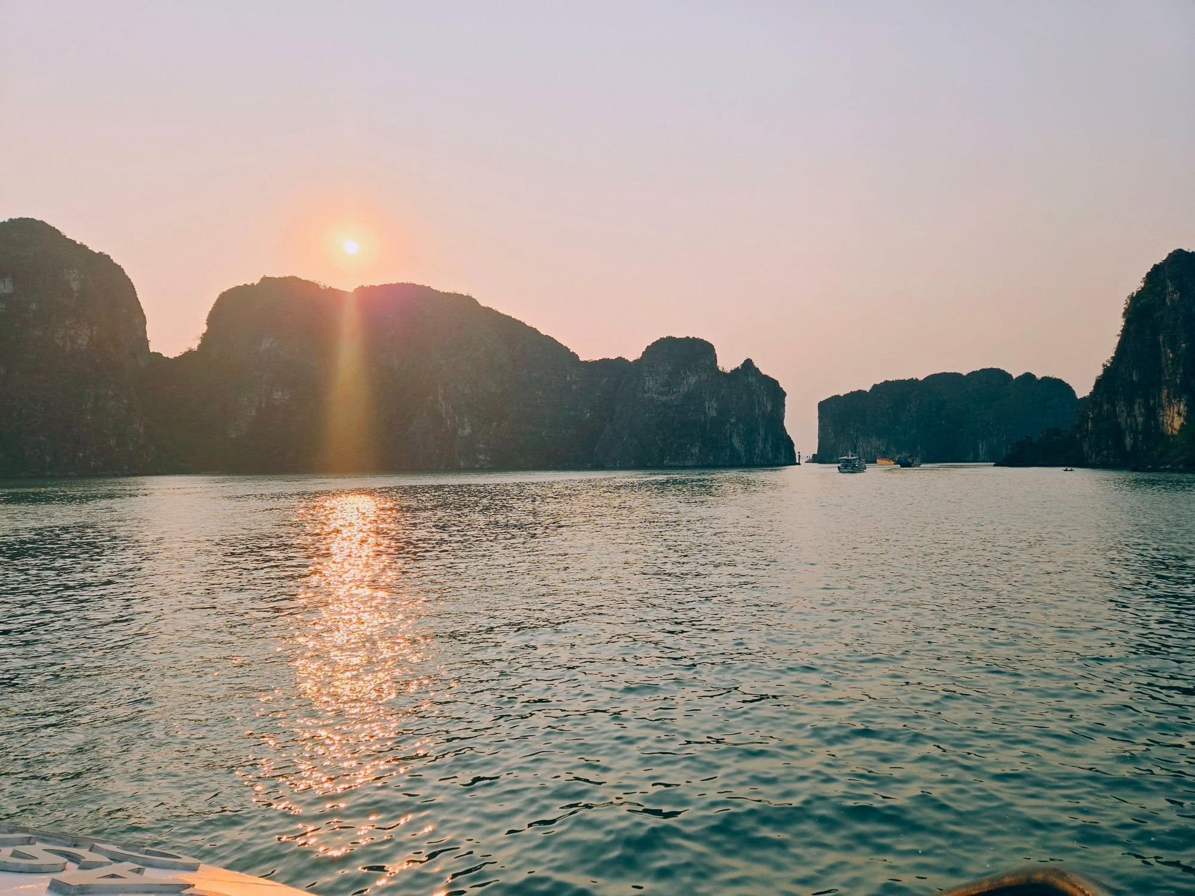 A golden sunset illuminates the limestone karsts of Ha Long Bay, Vietnam, with reflections shimmering on the calm waters.