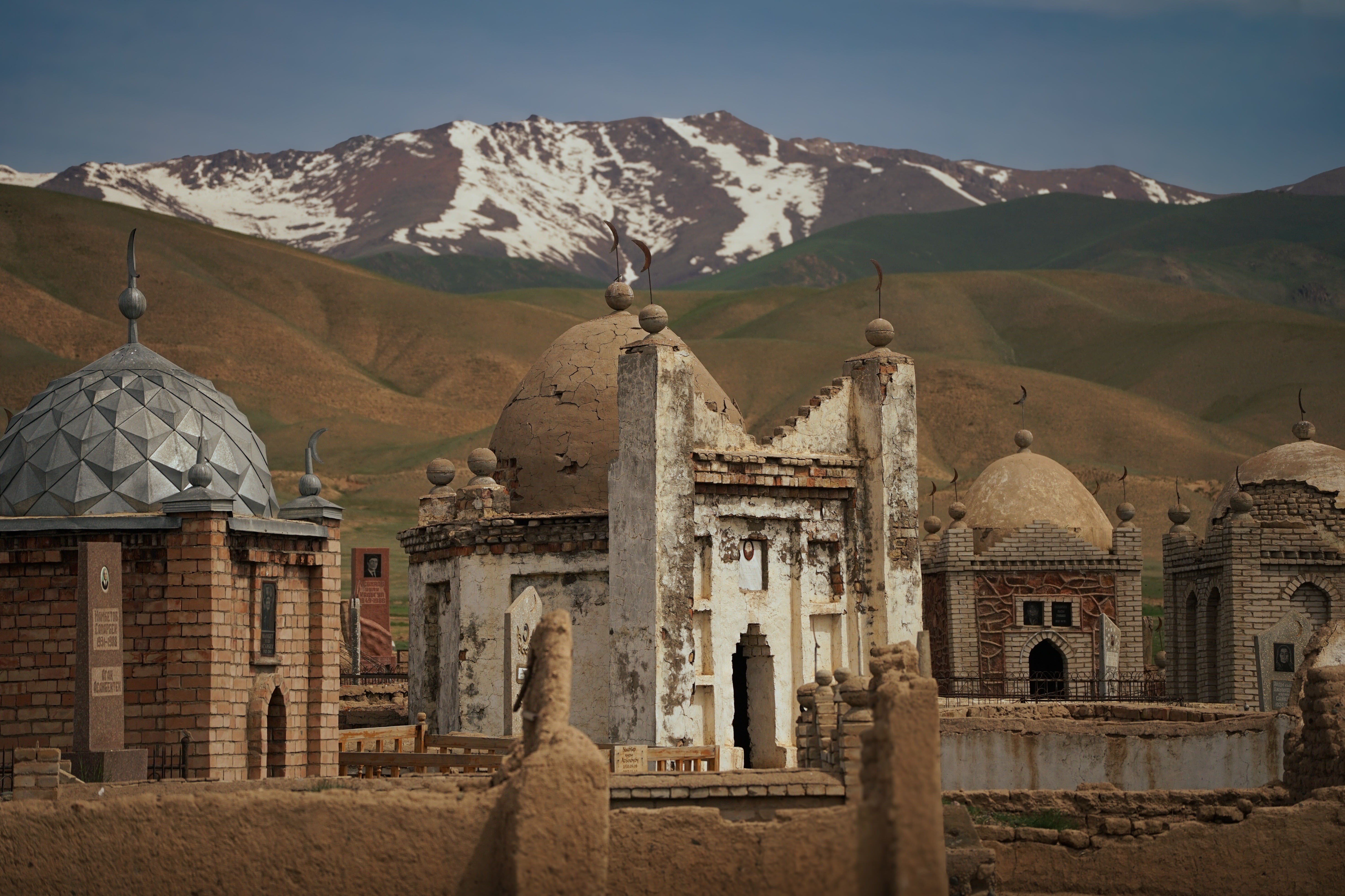 Historic mausoleums with domed structures set against the backdrop of the Tian Shan mountains in Kazakhstan.