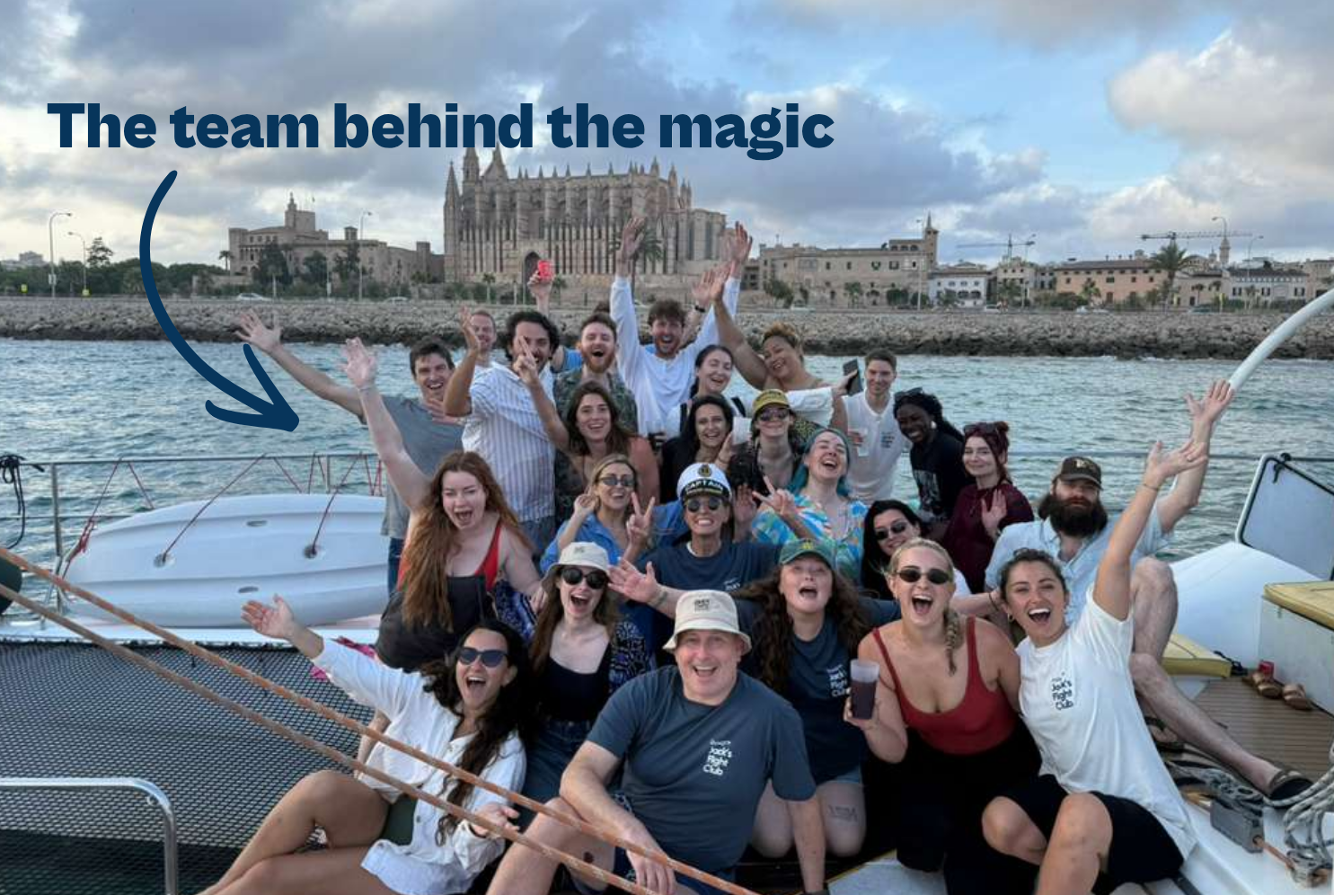 A joyful group poses on a boat with the stunning backdrop of La Seu Cathedral in Palma de Mallorca.