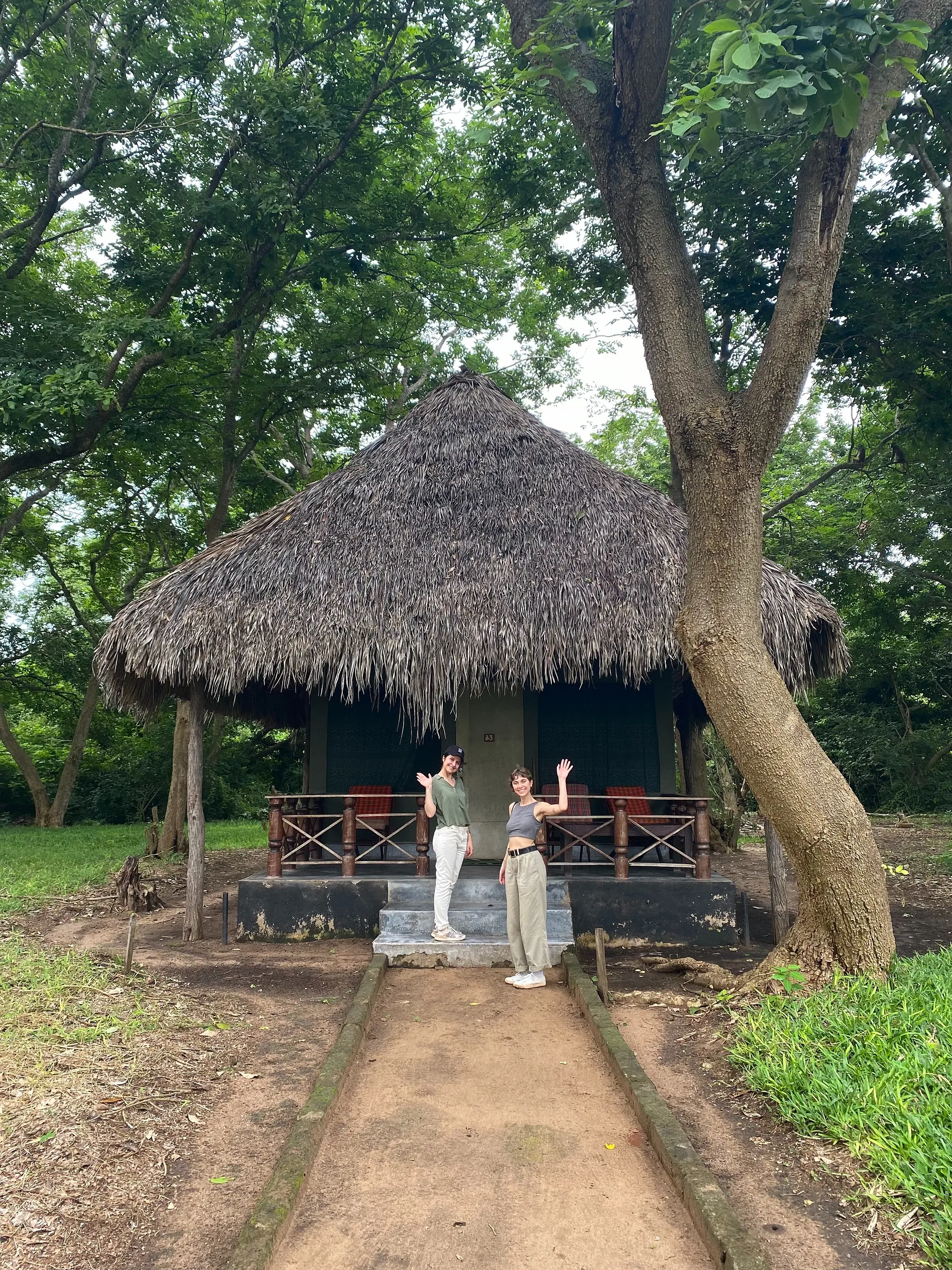 Fran and Andreia waving outside a hut