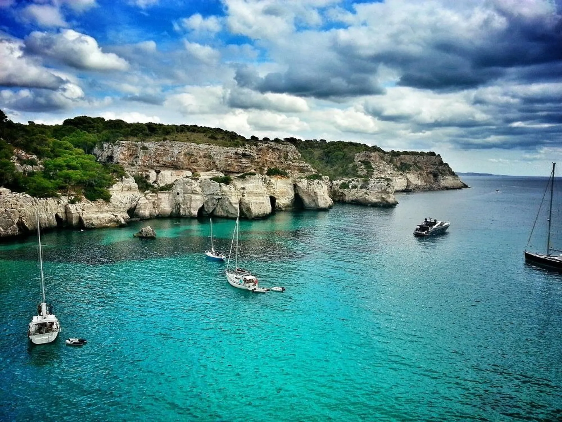 Sailboats and cliffs grace the turquoise waters of Cala Macarella in Menorca, Spain.