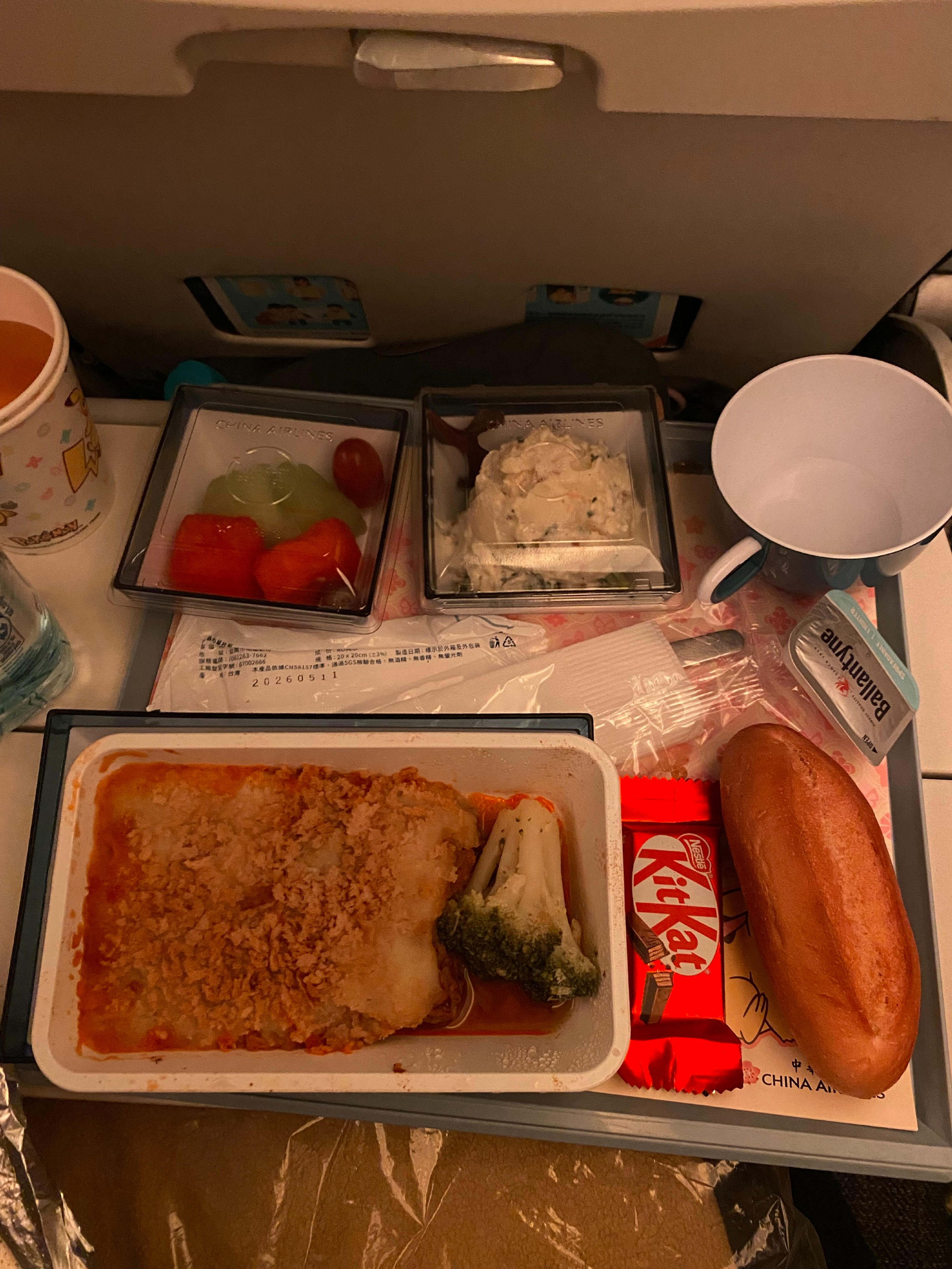 An in-flight meal served on China Airlines includes various food items like a main dish, salad, fruit, bread, and a Kit Kat chocolate bar on a tray.