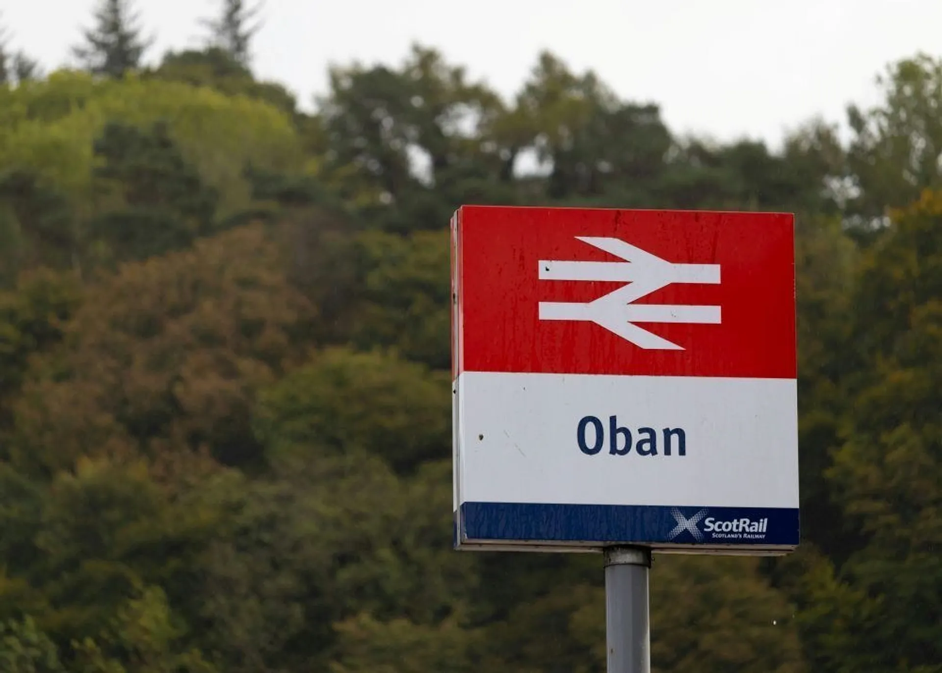 A ScotRail sign stands against a backdrop of lush greenery, marking the location of Oban in Scotland.