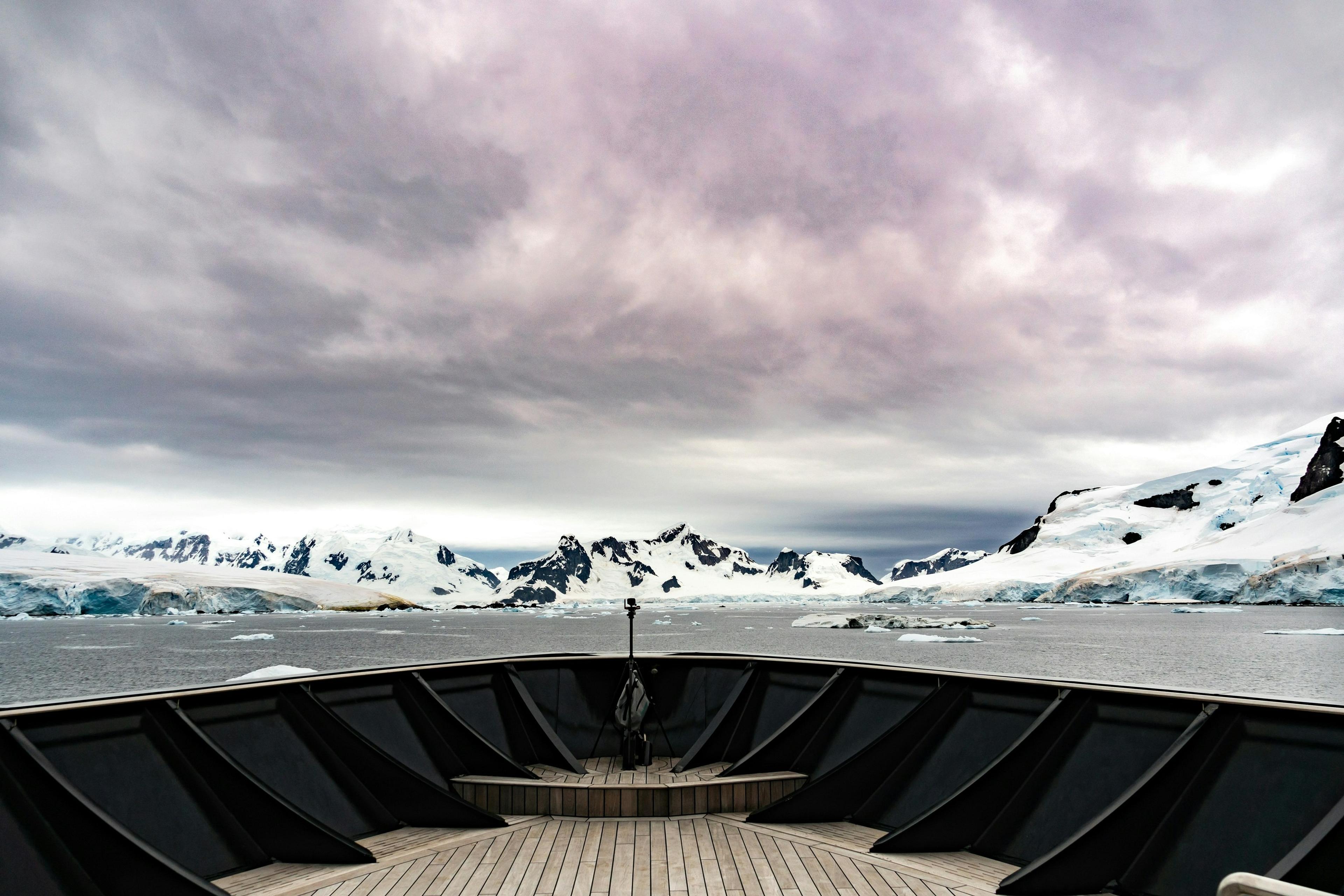 A ship's deck overlooks the icy landscape of Paradise Bay in Antarctica under a moody sky.