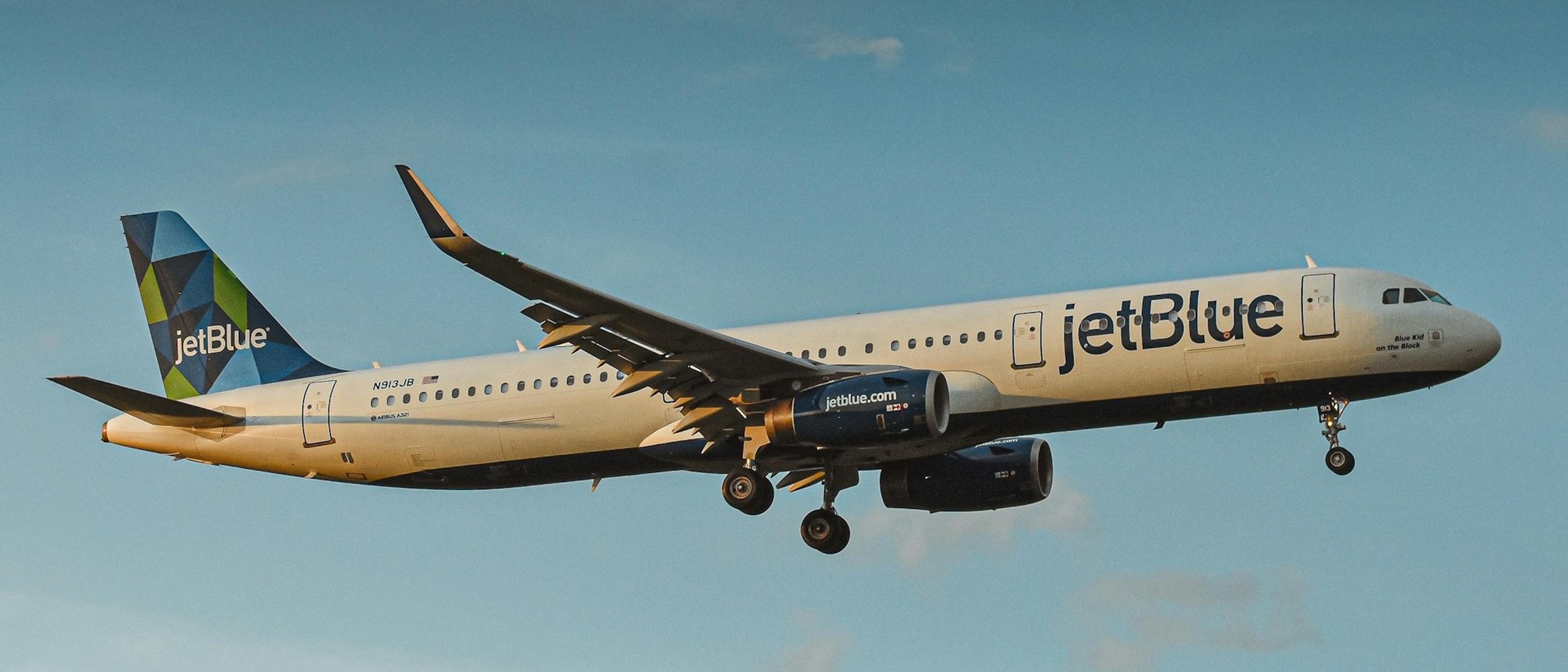 A JetBlue airplane prepares for landing, viewed against a clear blue sky.