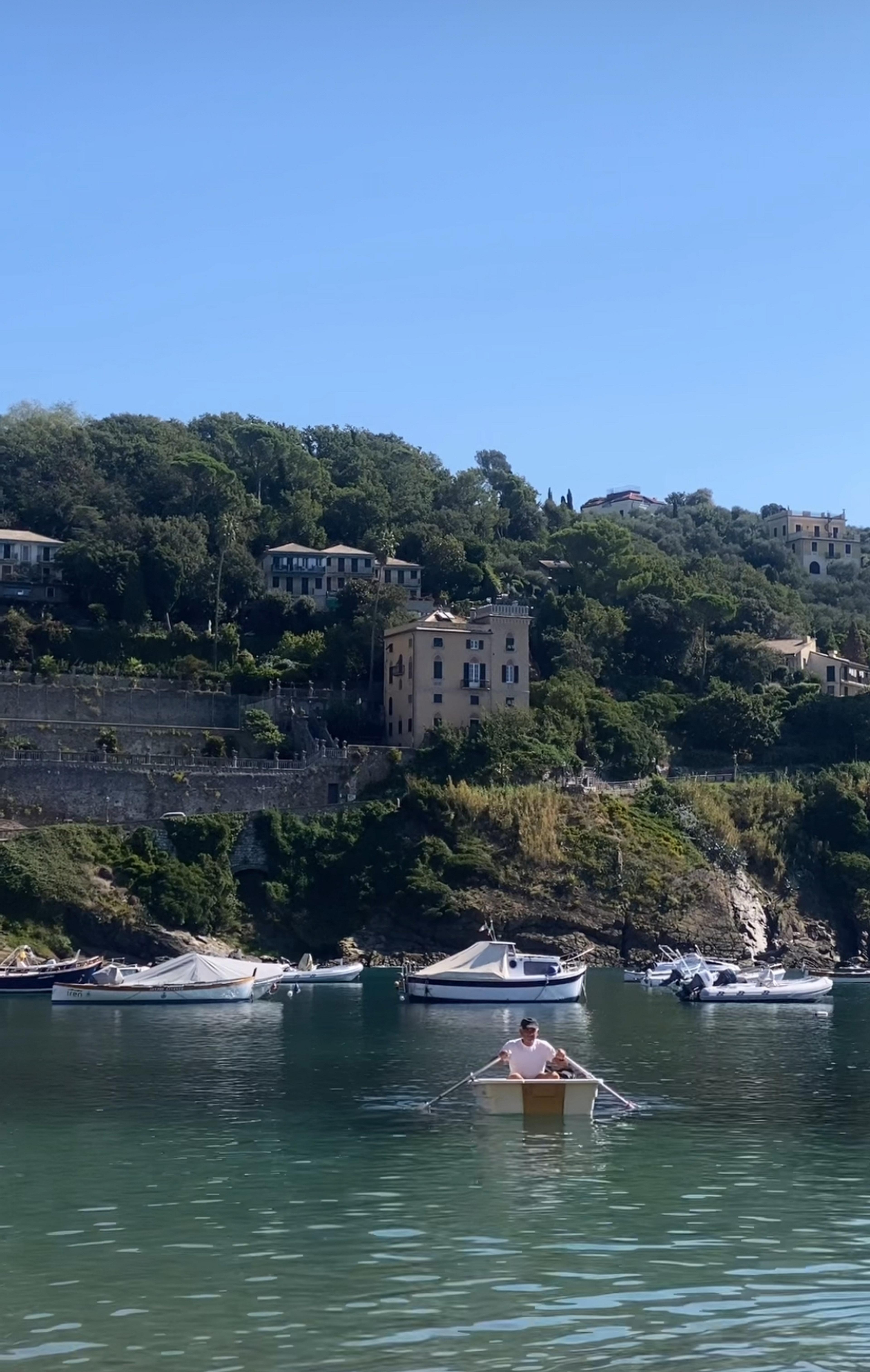 A man rows a boat in the tranquil waters of Sestri Levante, Italy, with picturesque hillside villas in the background.
