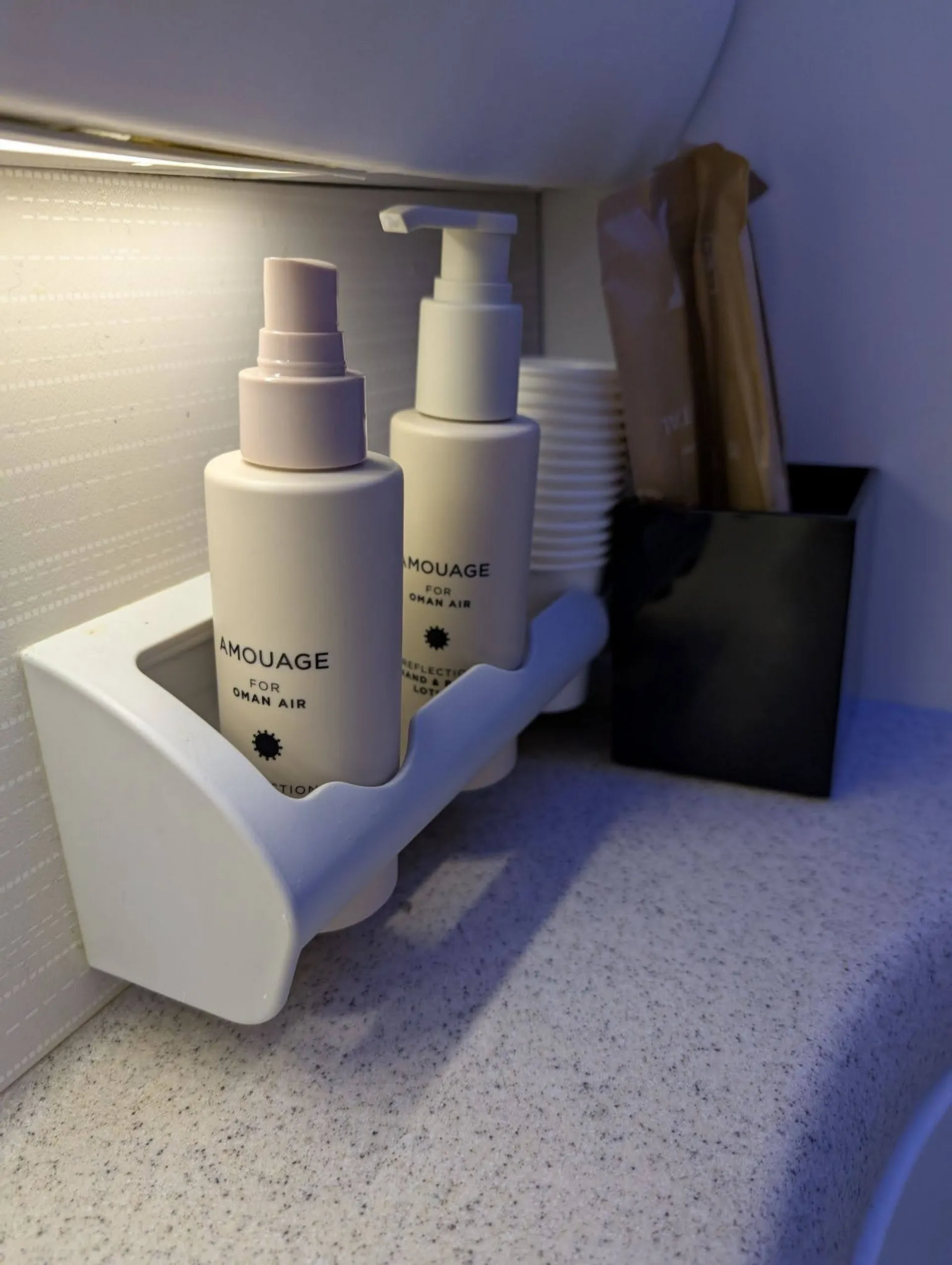 A compact shelf in an Oman Air airplane restroom contains Amouage products.