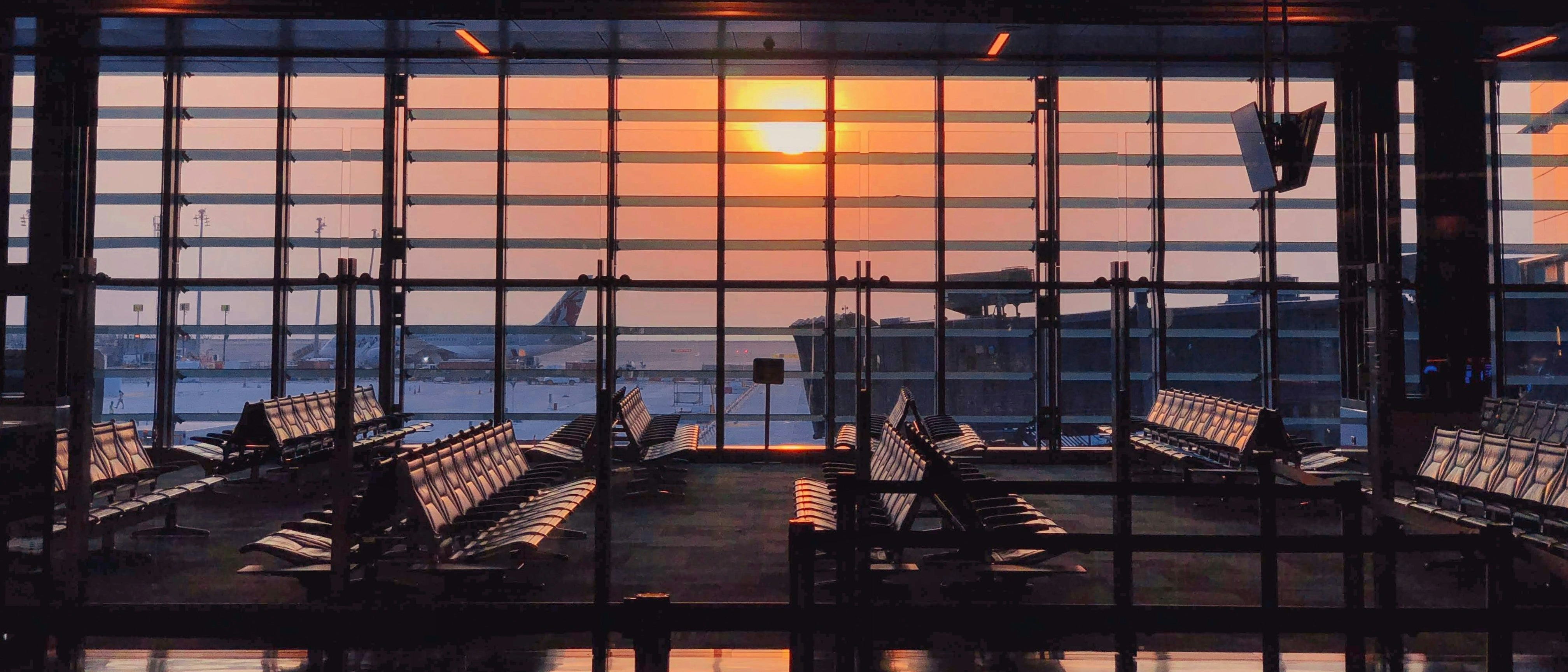 A sunlit departure lounge at Hamad International Airport in Doha features rows of empty seats and a view of aircraft through the expansive windows.