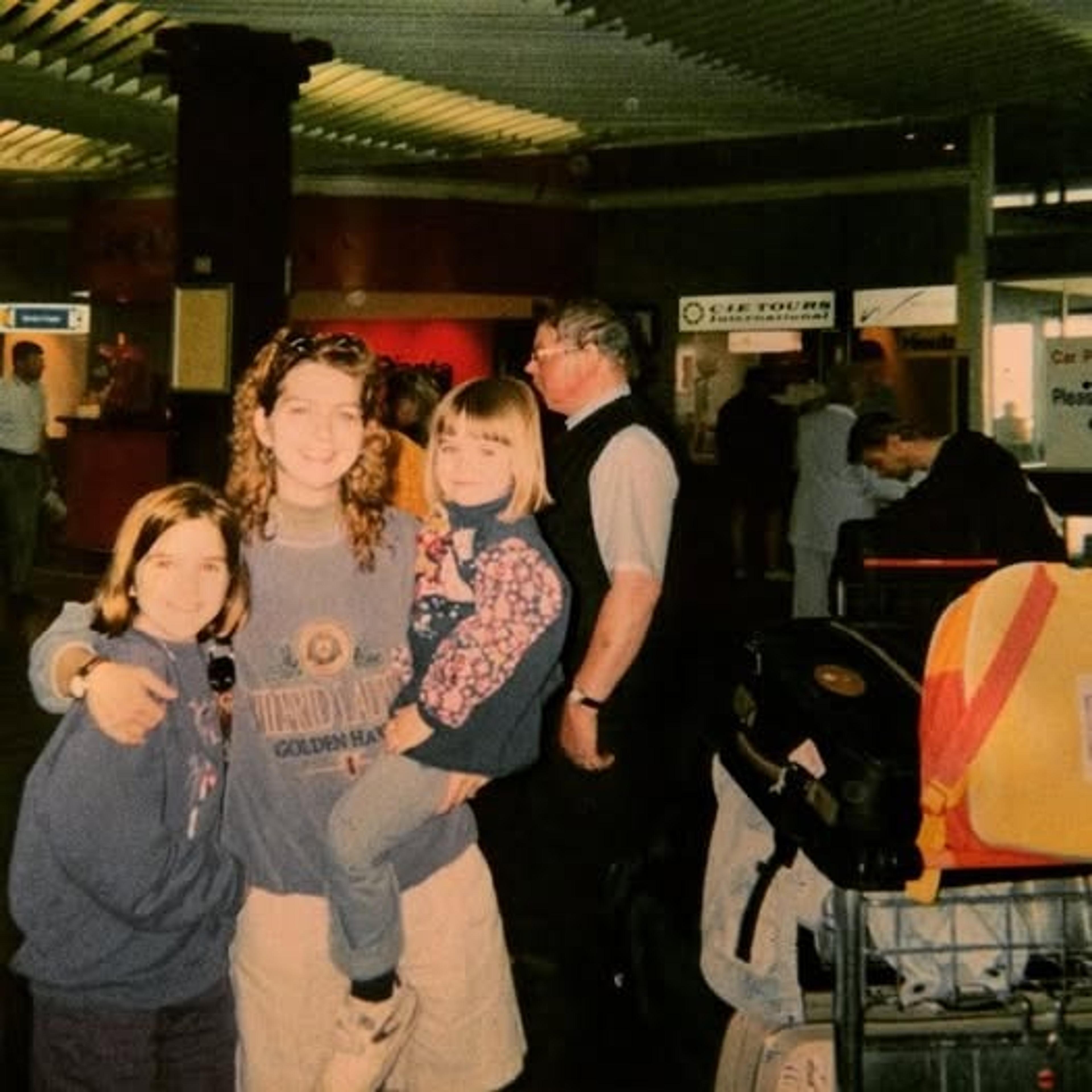 A group of people pose for a photo inside Gatwick Airport, surrounded by suitcases and signs for travel services.