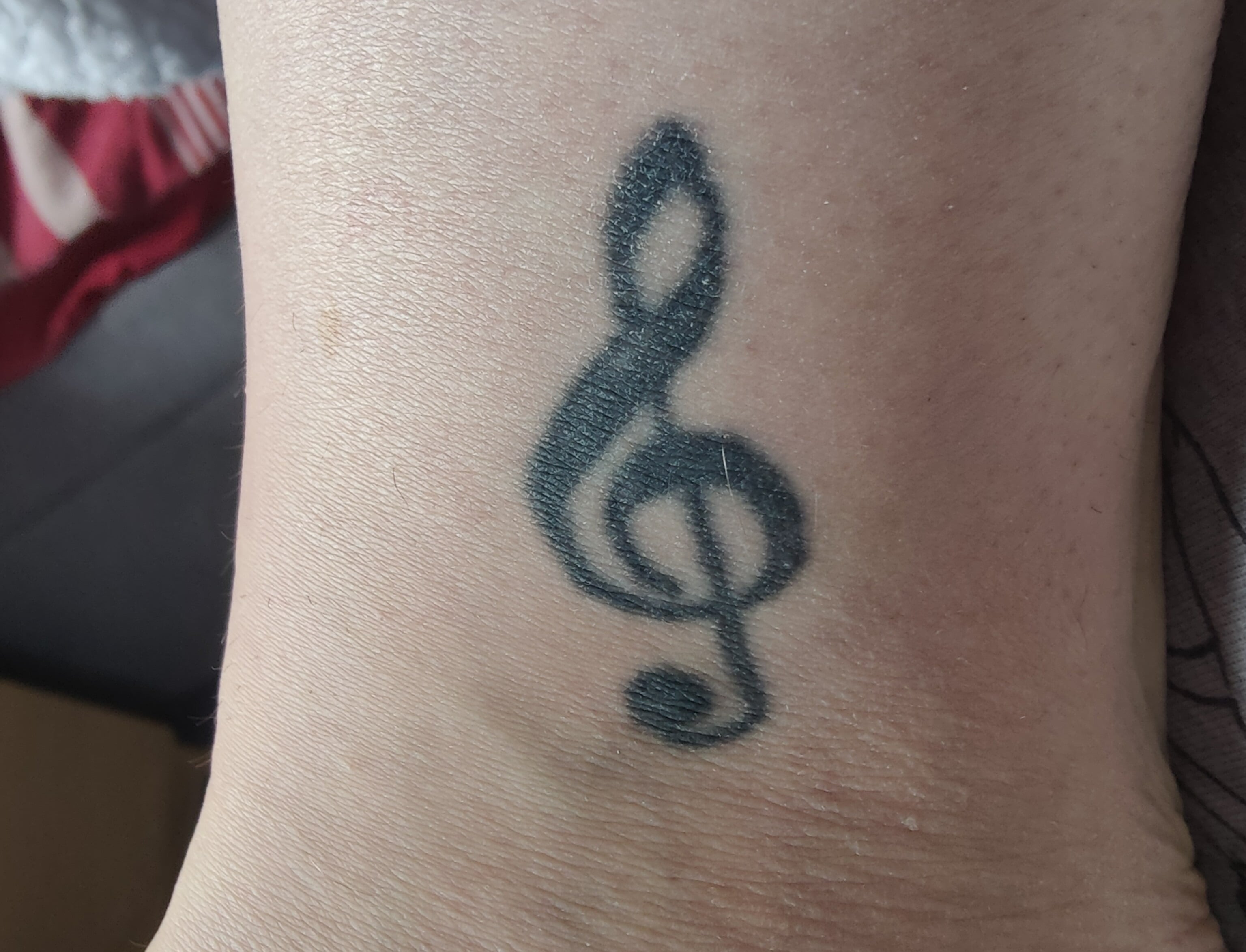 A tattoo of a treble clef adorns the skin.