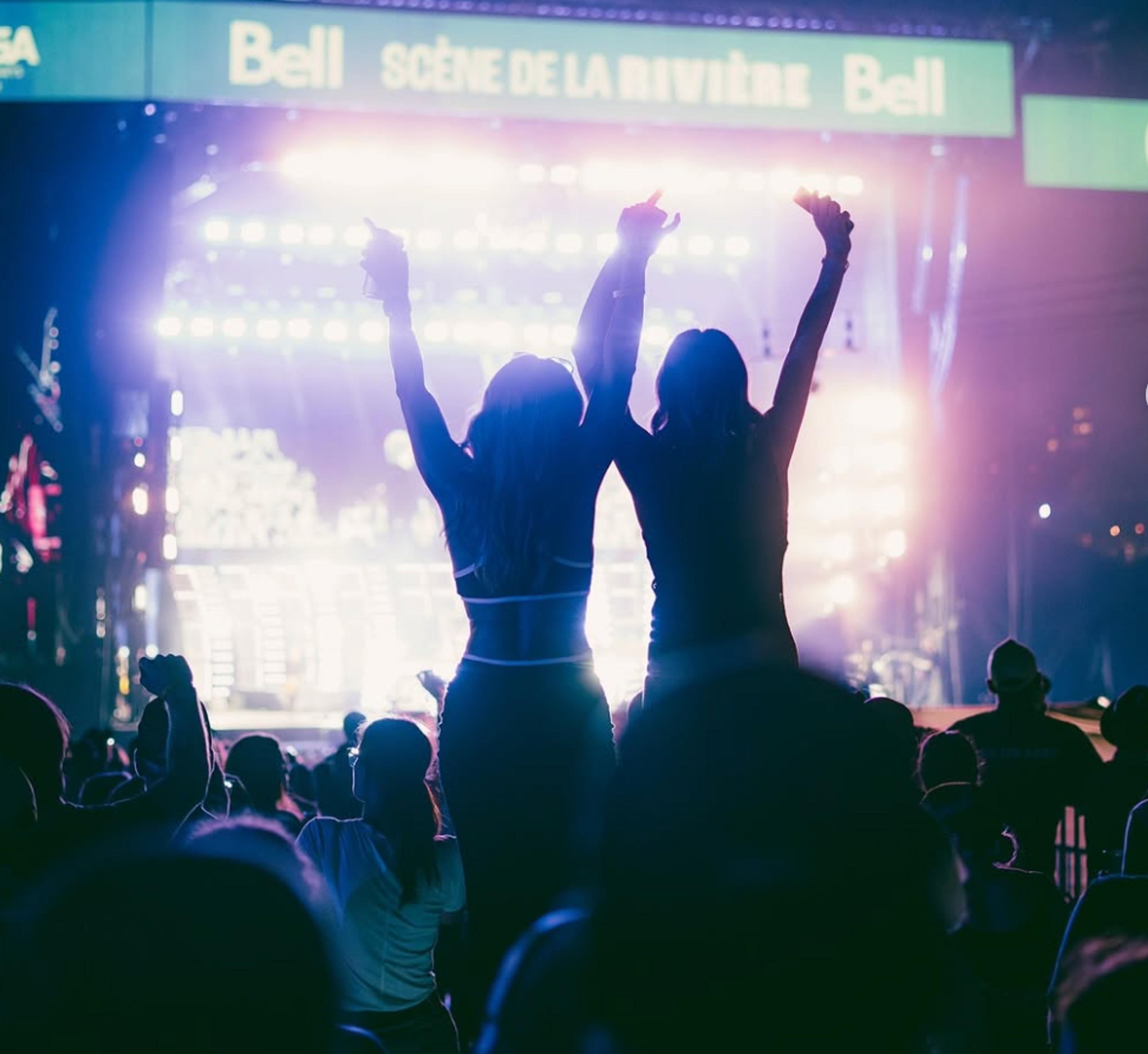 Two women backlit, dancing in front of a bright stage.