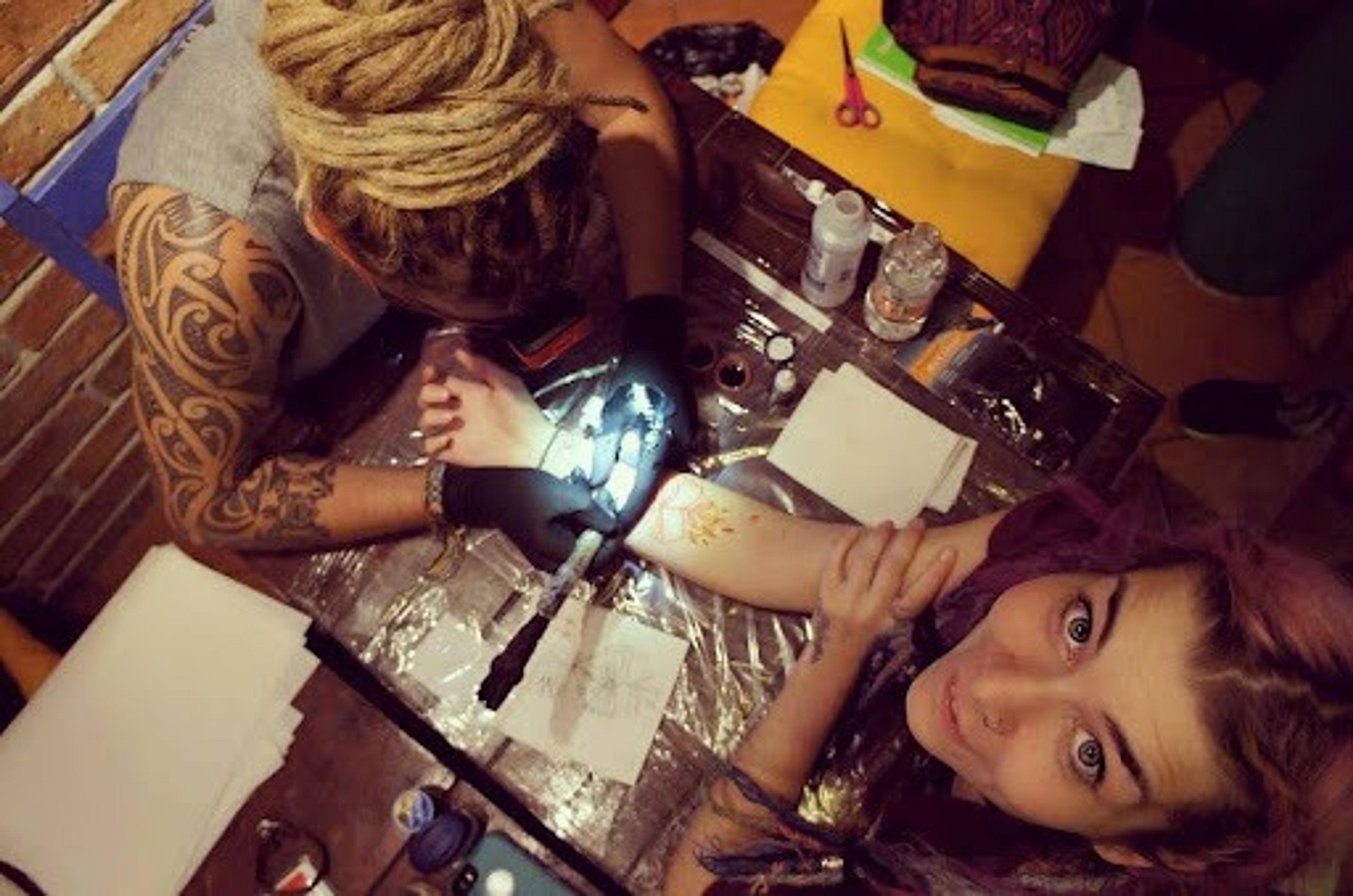 A person gets a tattoo in a studio, viewed from above, with detailed attention to the intricate ink design.