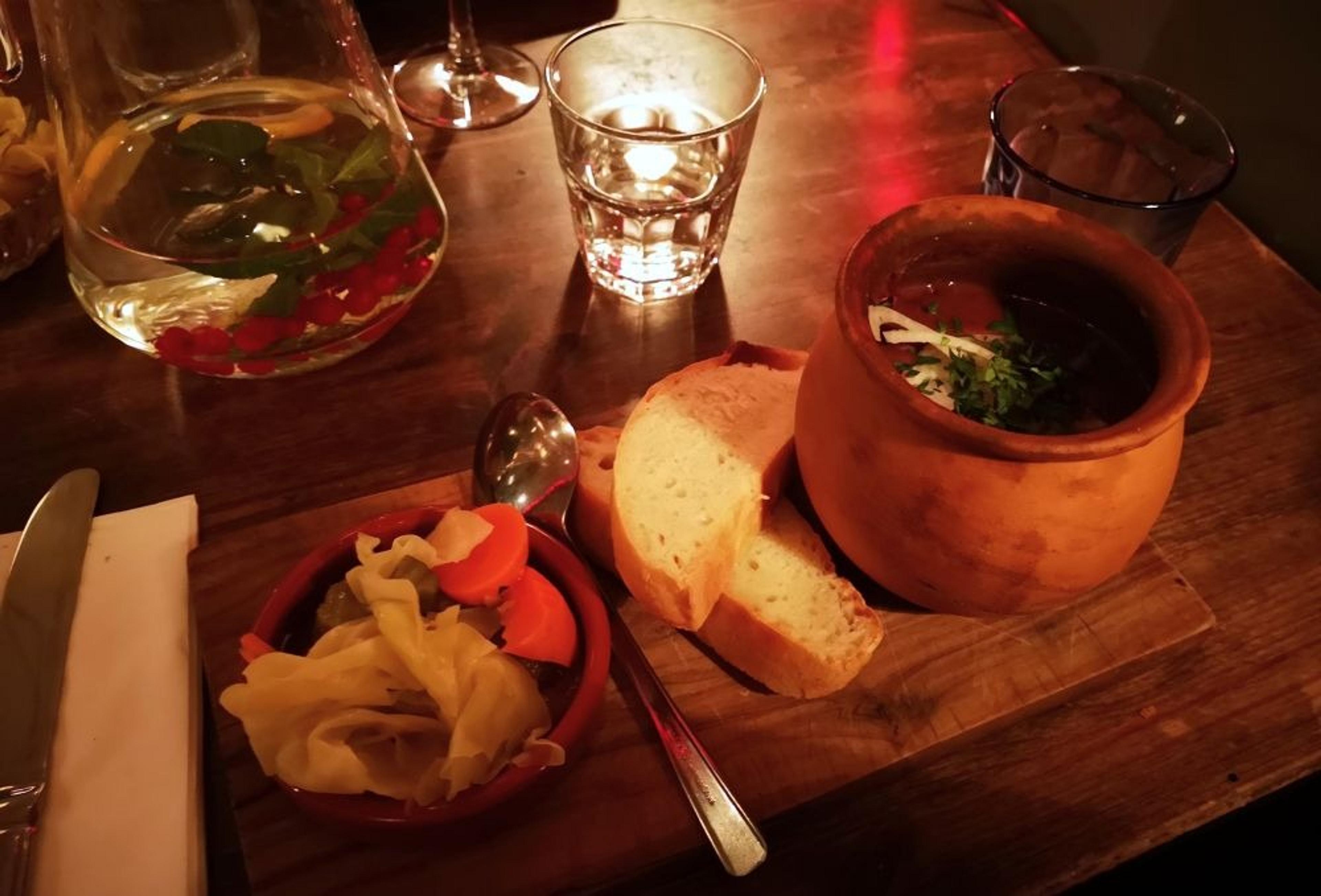 A cozy restaurant setting, features a traditional clay pot dish with bread and pickled vegetables on a wooden table.