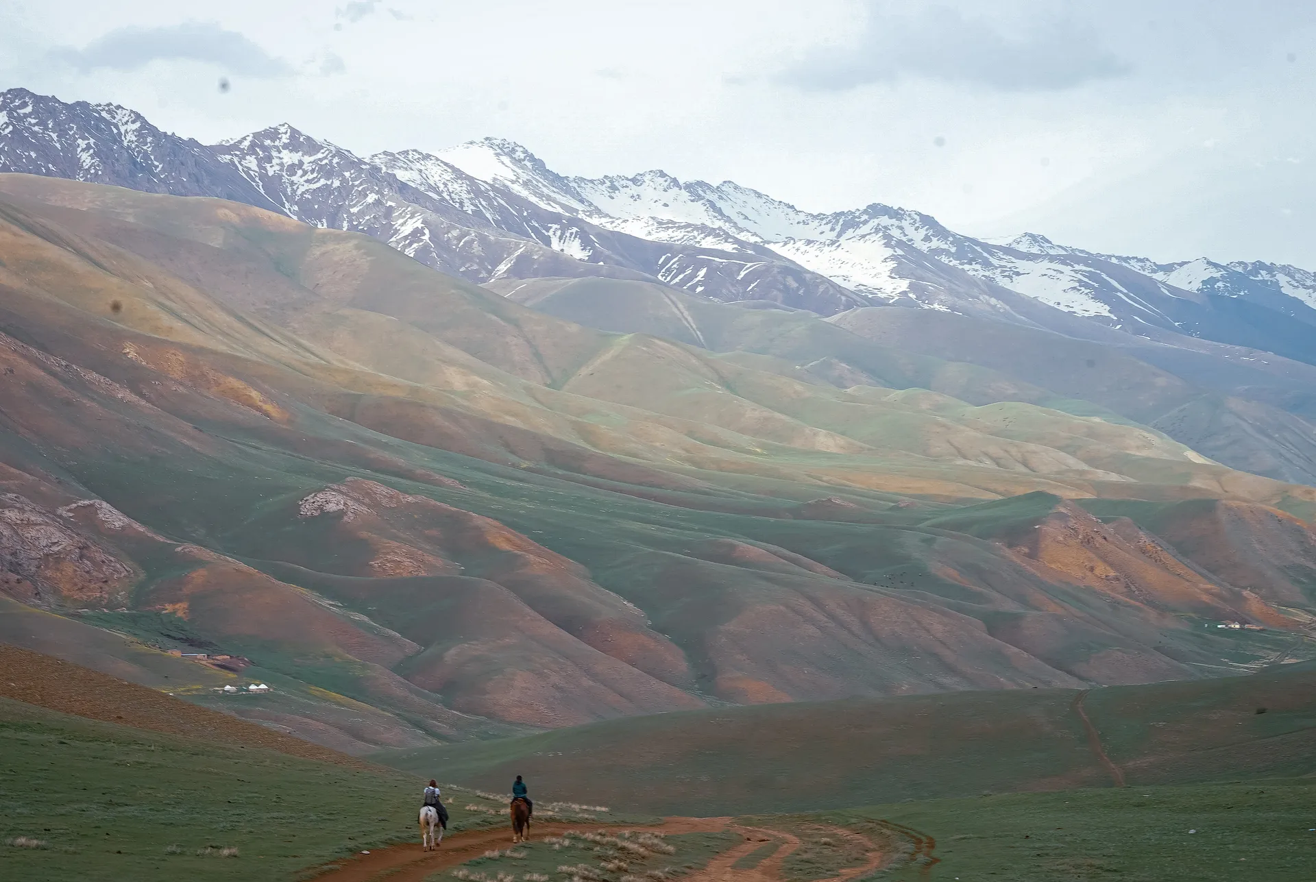 Two horseback riders traverse the rolling hills near the Tian Shan mountains in Kyrgyzstan.