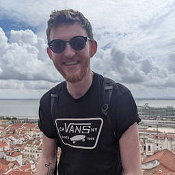 A person smiles in front of Lisbon's scenic red rooftops overlooking the Tagus River.