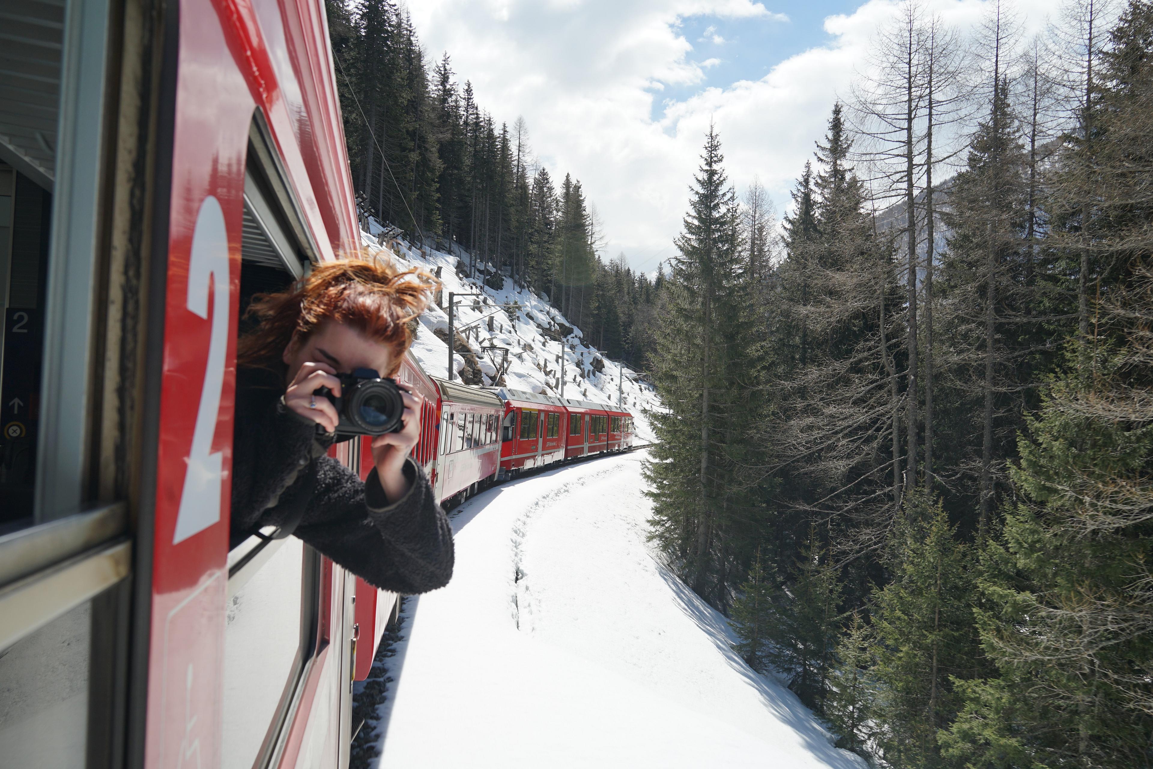 A passenger captures photos from a red train winding through the snowy Swiss Alps.