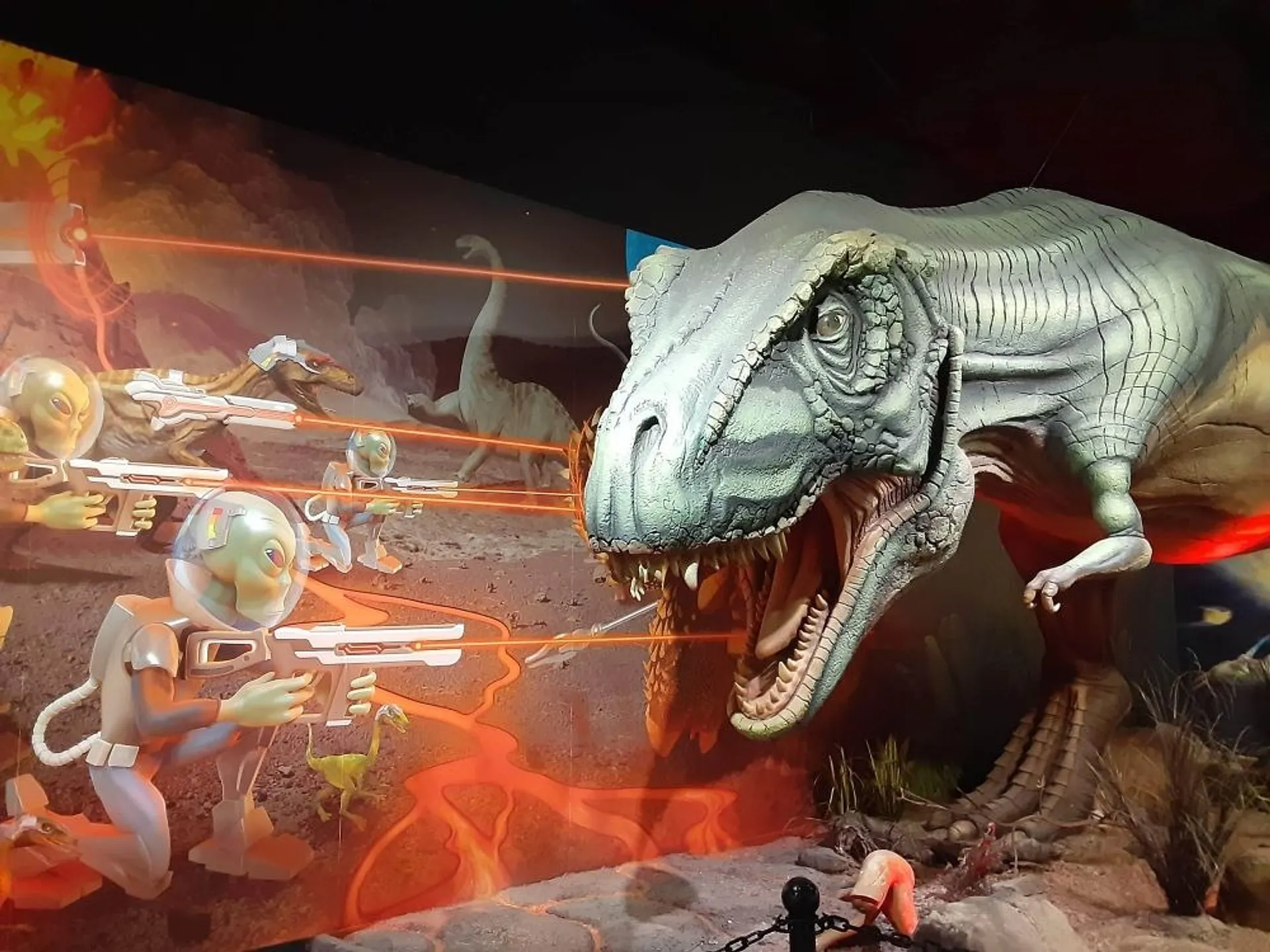 Huge T-Rex model in front of an image of aliens shooting towards it