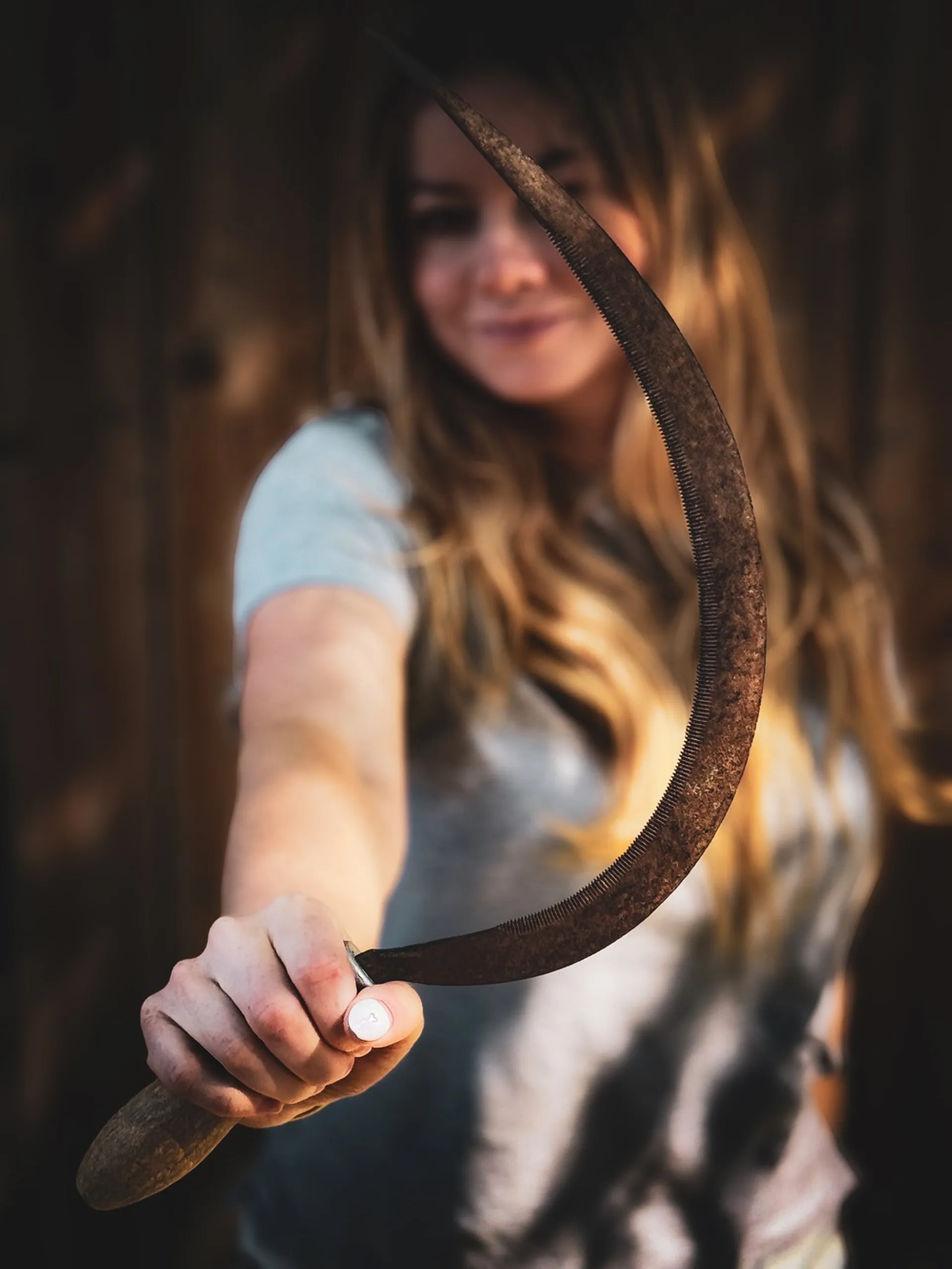 Flight Finder Kristi holding a curved rusty sickle is standing in front of a wooden backdrop.