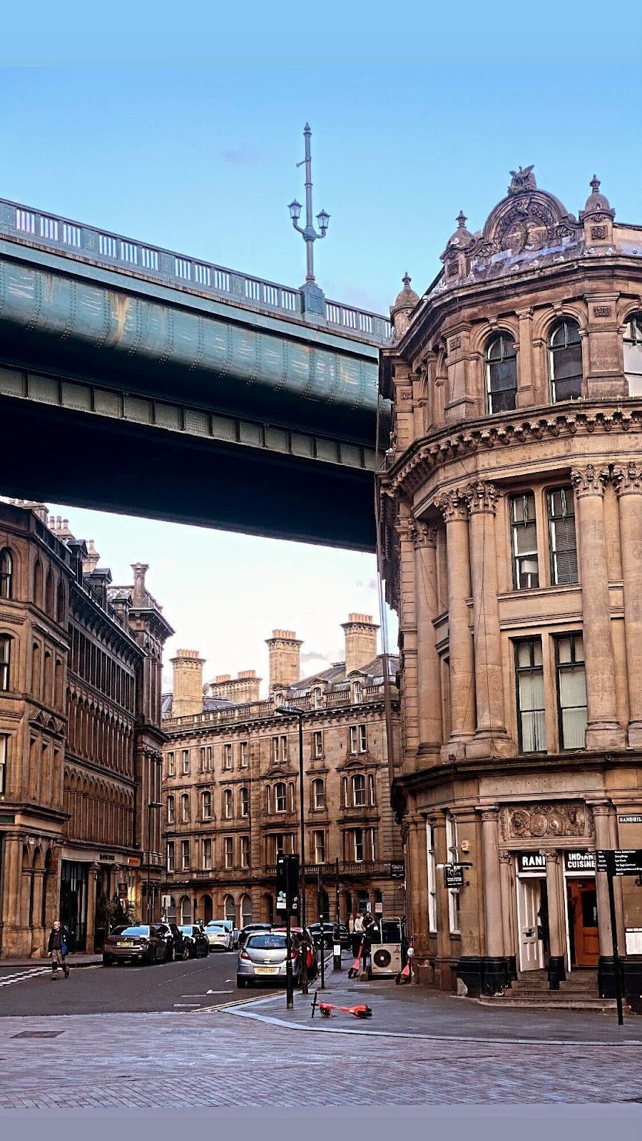 Terraced sandstone buildings on a cobbled street with a bridge overhead