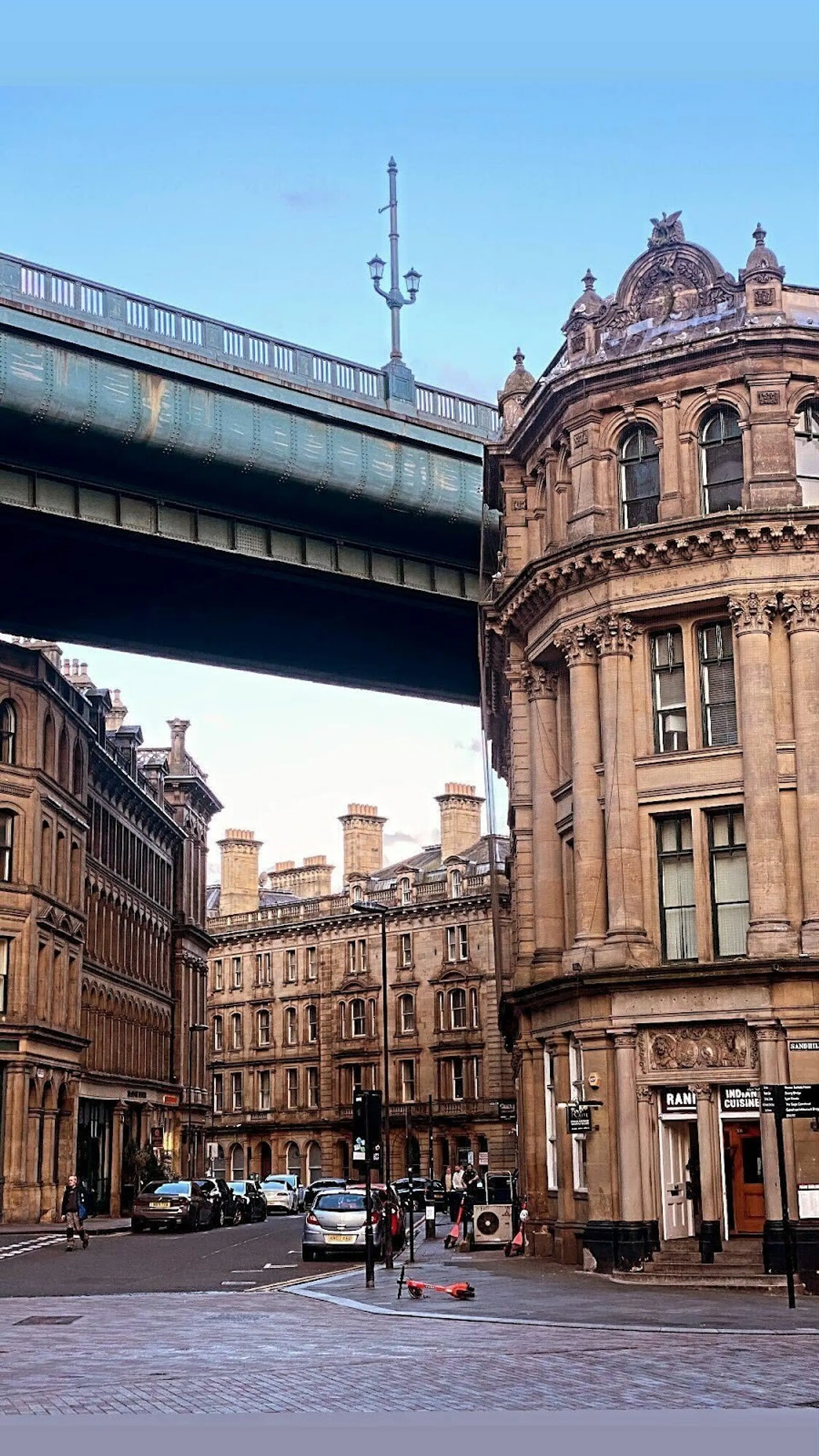 Terraced sandstone buildings on a cobbled street with a bridge overhead