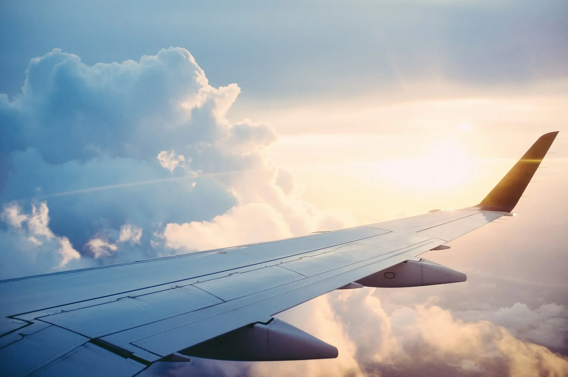 An airplane wing gliding above fluffy clouds during a serene sunset at cruising altitude.