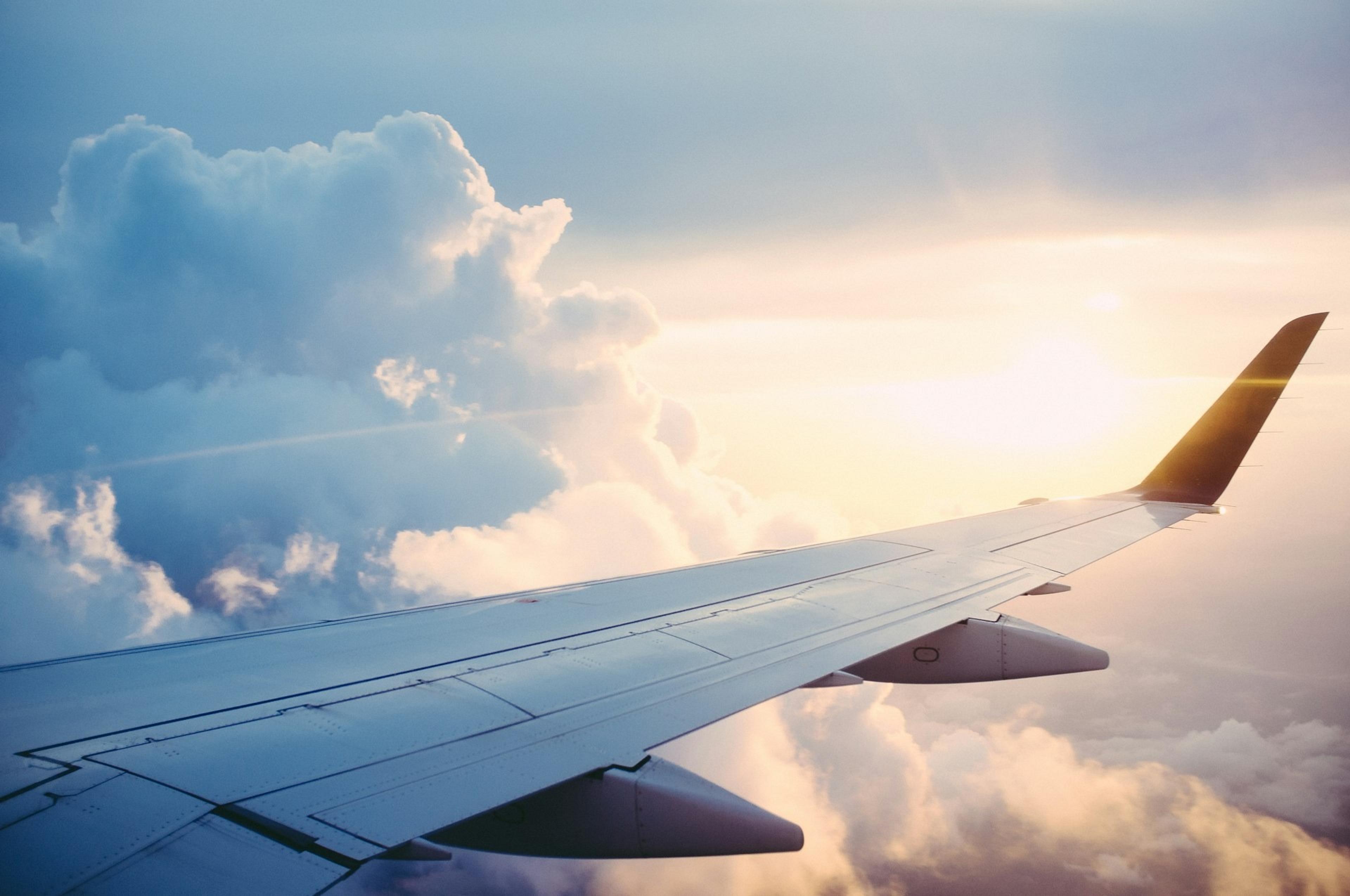 An airplane wing gliding above fluffy clouds during a serene sunset at cruising altitude.