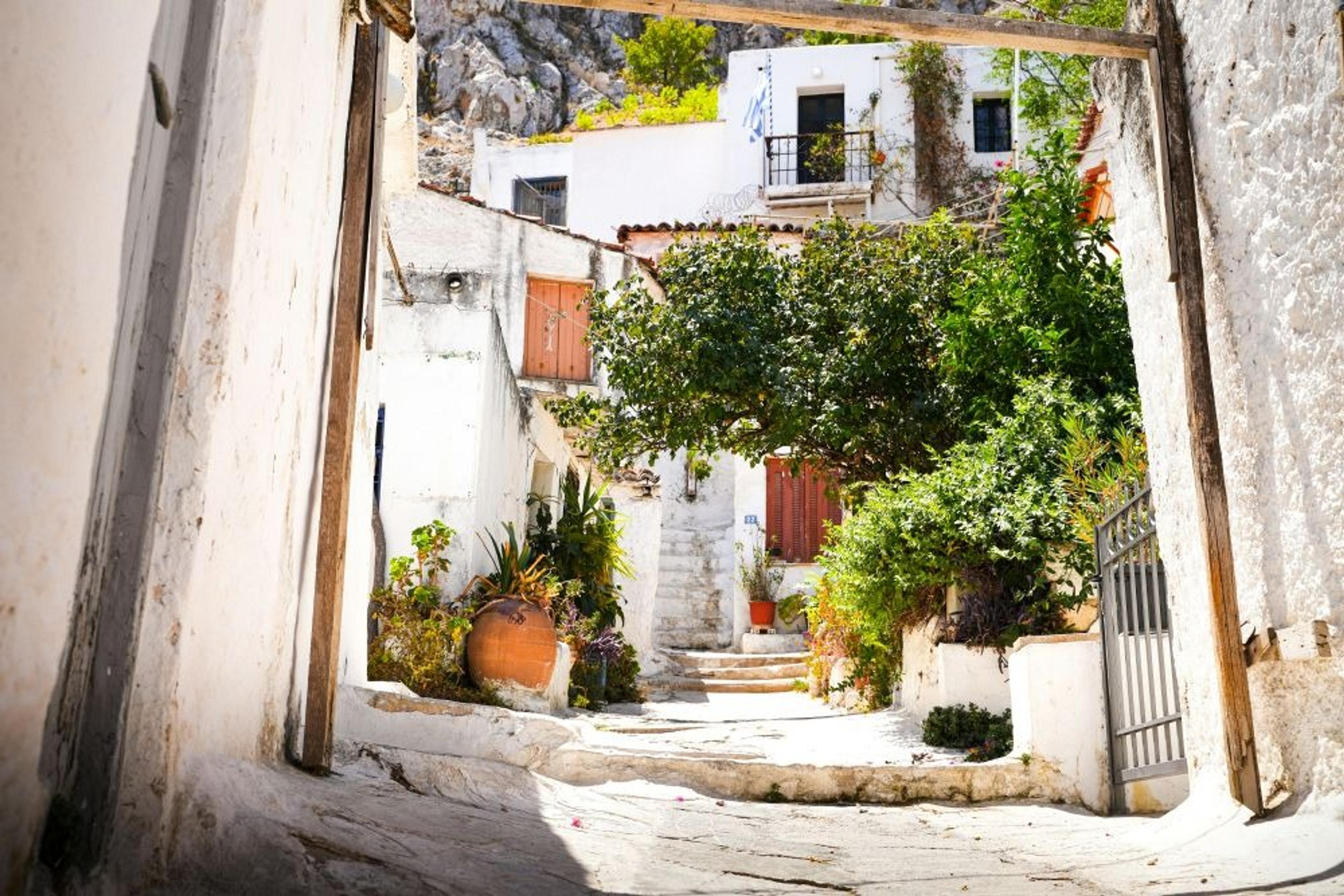 A charming alleyway in Anafiotika, Athens, lined with whitewashed buildings and lush greenery, captures the essence of a quaint Greek village.