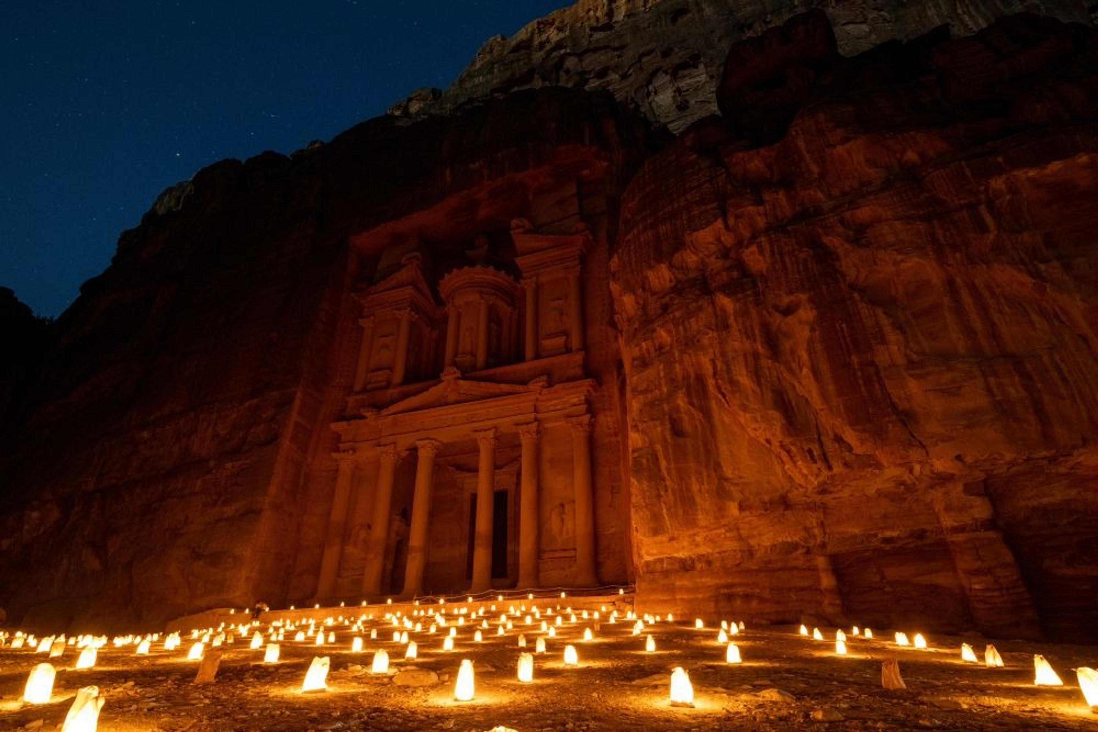 Candles illuminate the ancient rock-carved facade of Al-Khazneh in Petra, Jordan, under a starlit night sky.
