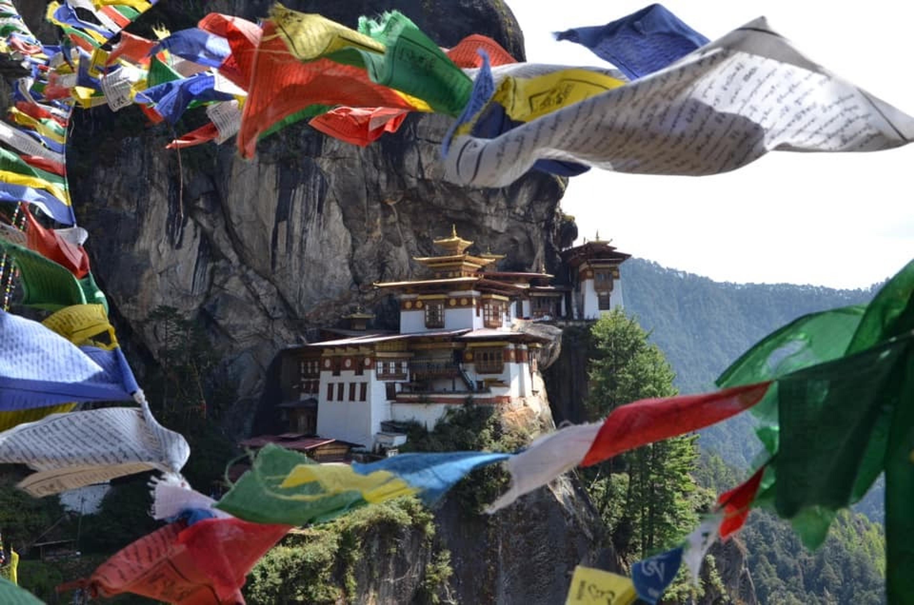 Paro Taktsang, also known as the Tiger's Nest Monastery, clings to a cliff in Bhutan, accompanied by vibrant prayer flags fluttering in the foreground.