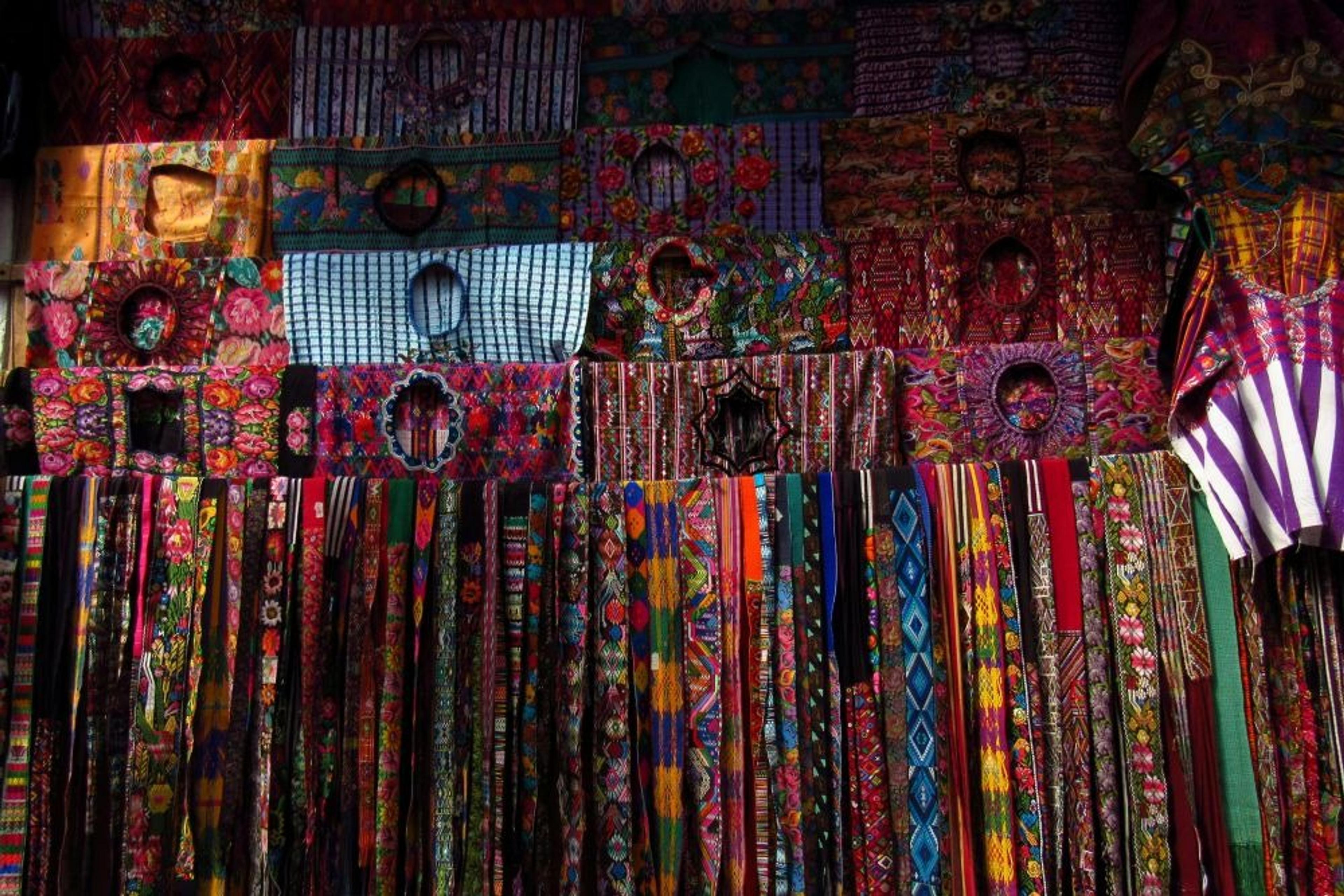 Vibrant Mayan textiles showcasing intricate patterns hang side by side in a traditional market stall in Guatemala.