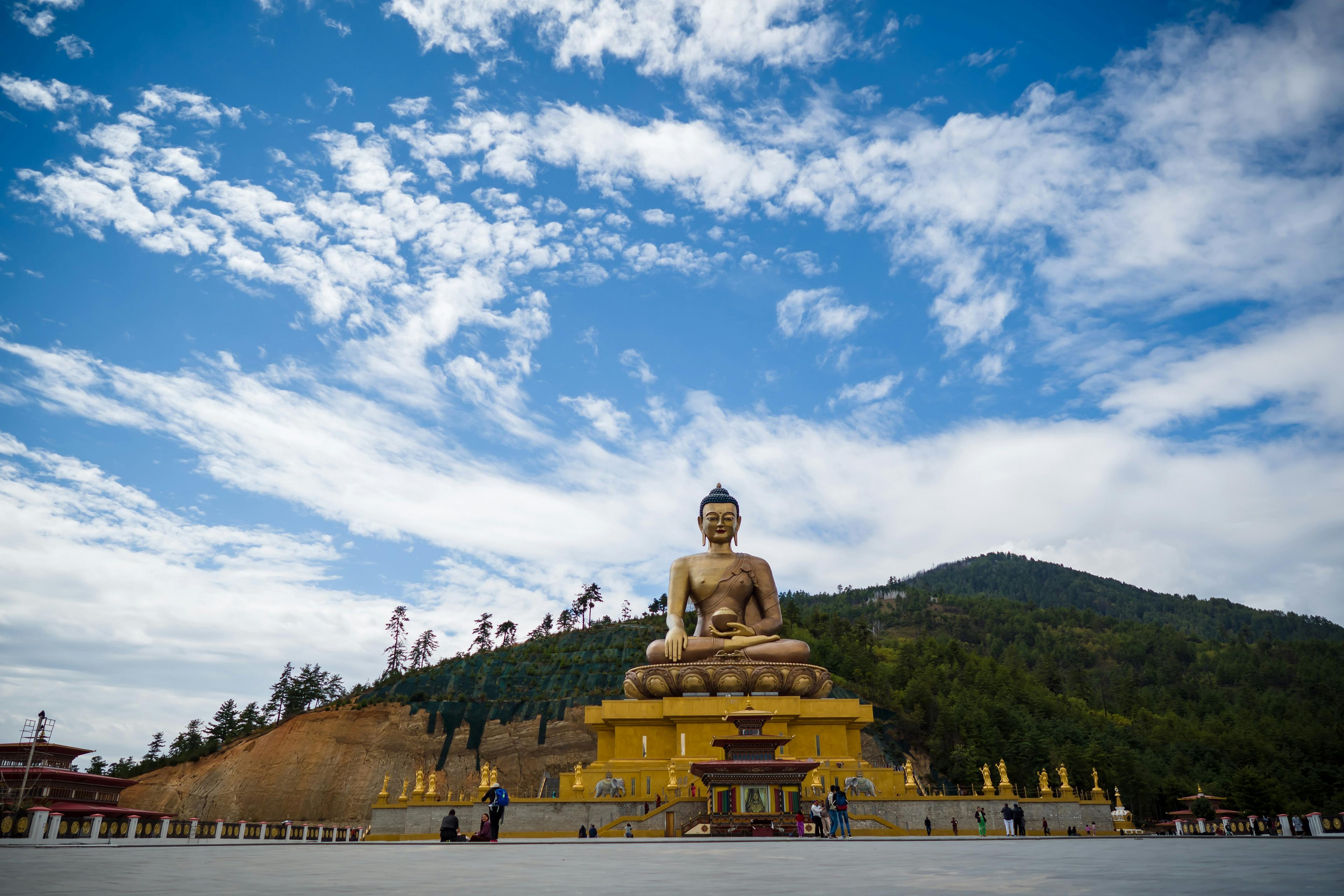 A magnificent golden Buddha statue sits prominently at Buddha Point (Kuensel Phodrang) in Thimphu, Bhutan, with lush hills and a vibrant sky as the backdrop.