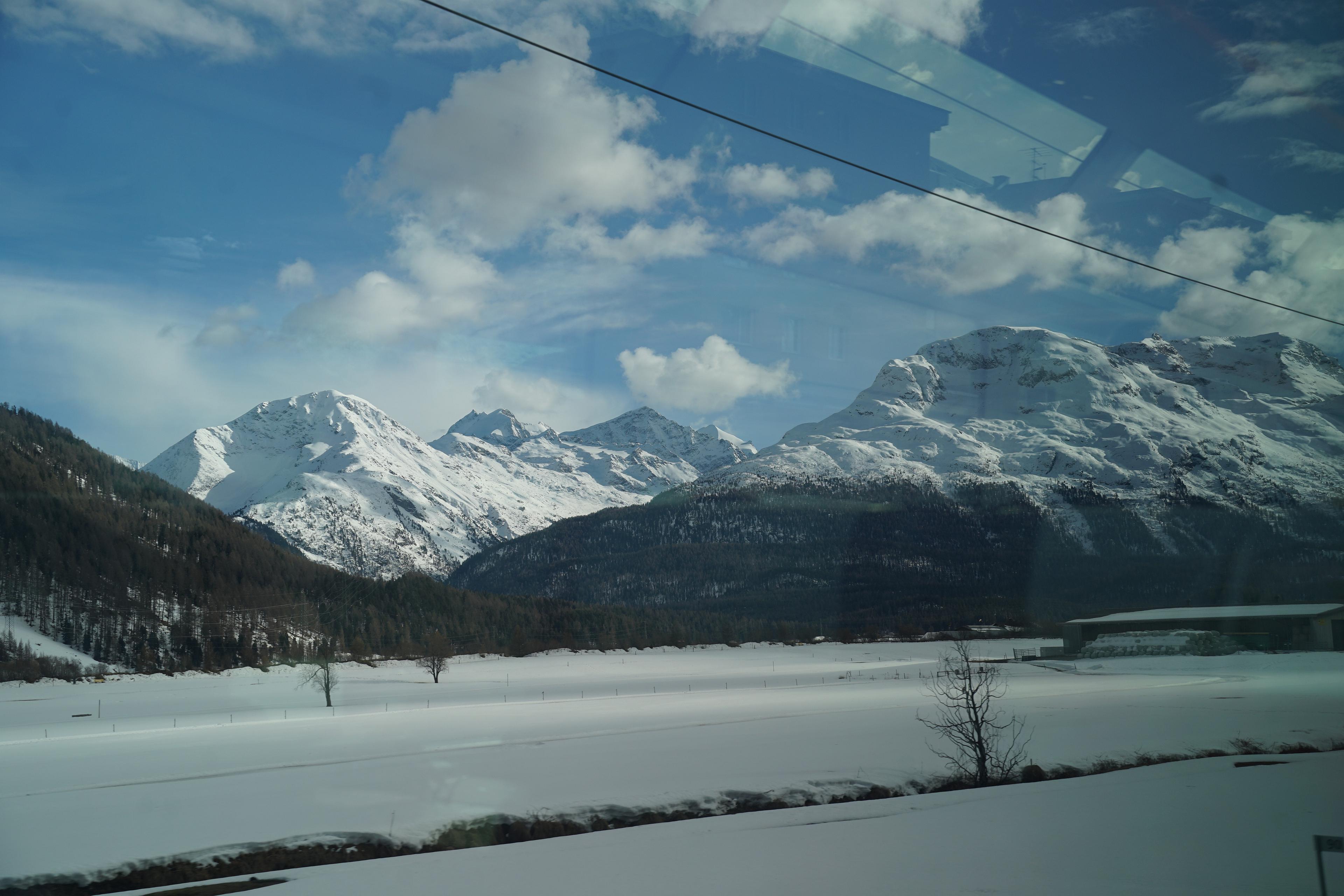 Snowy mountains and a serene landscape reflected in a window near St. Moritz, Switzerland.