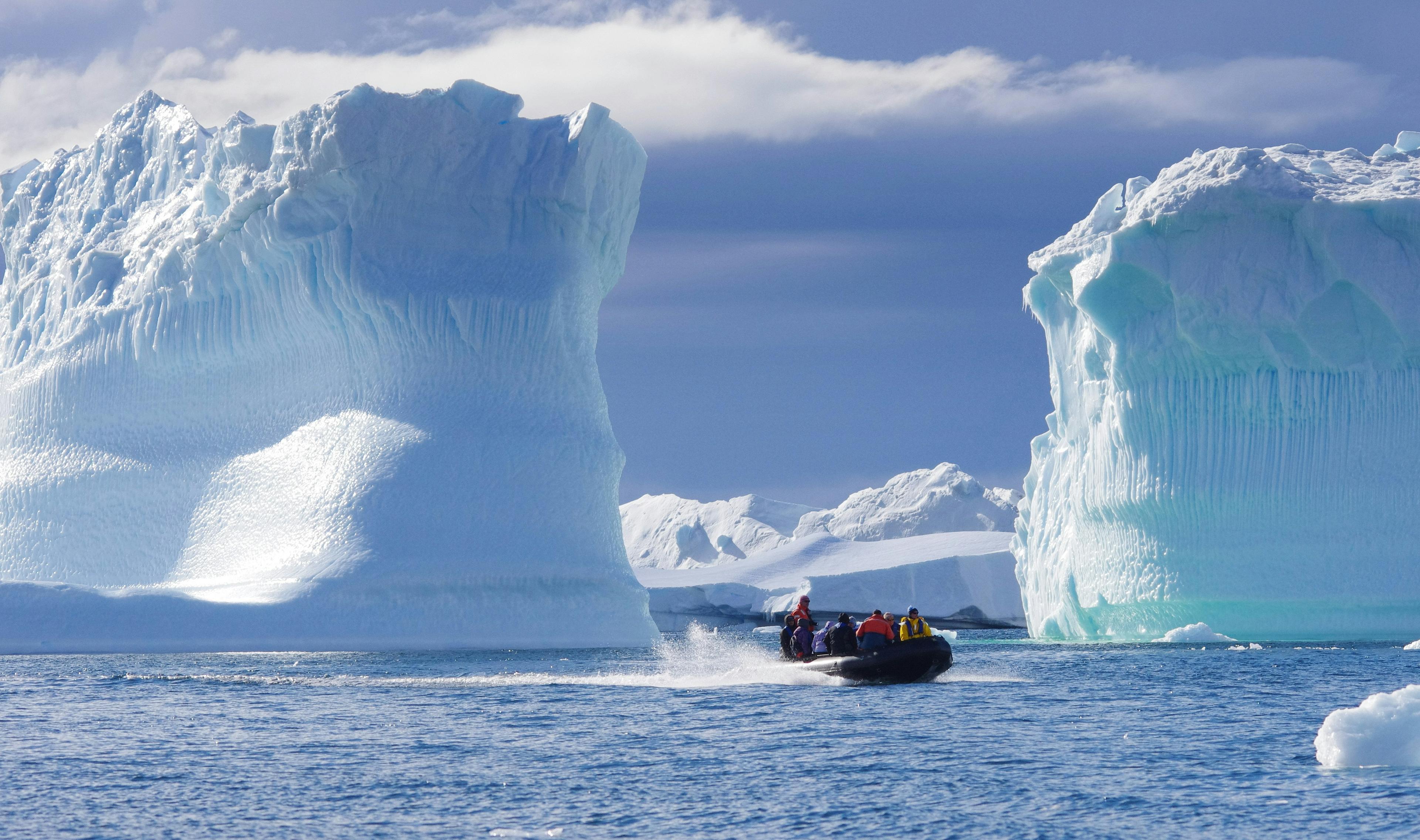 A small boat navigates between towering icebergs in the icy waters of Antarctica.