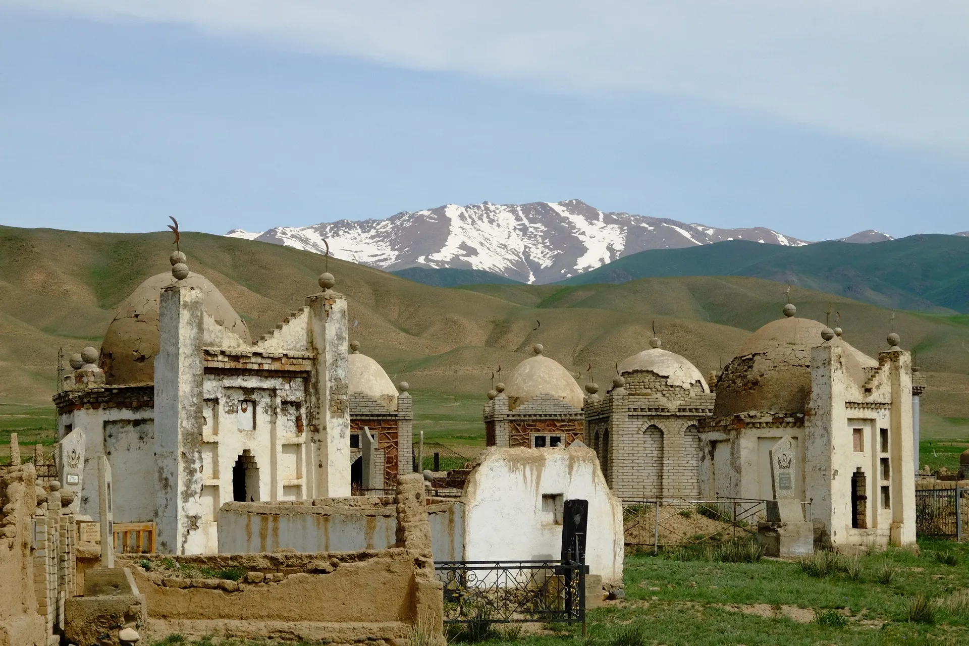 Historic mazars with domed structures stand against the backdrop of the snowy peaks of the Tien Shan mountains in Kyrgyzstan.