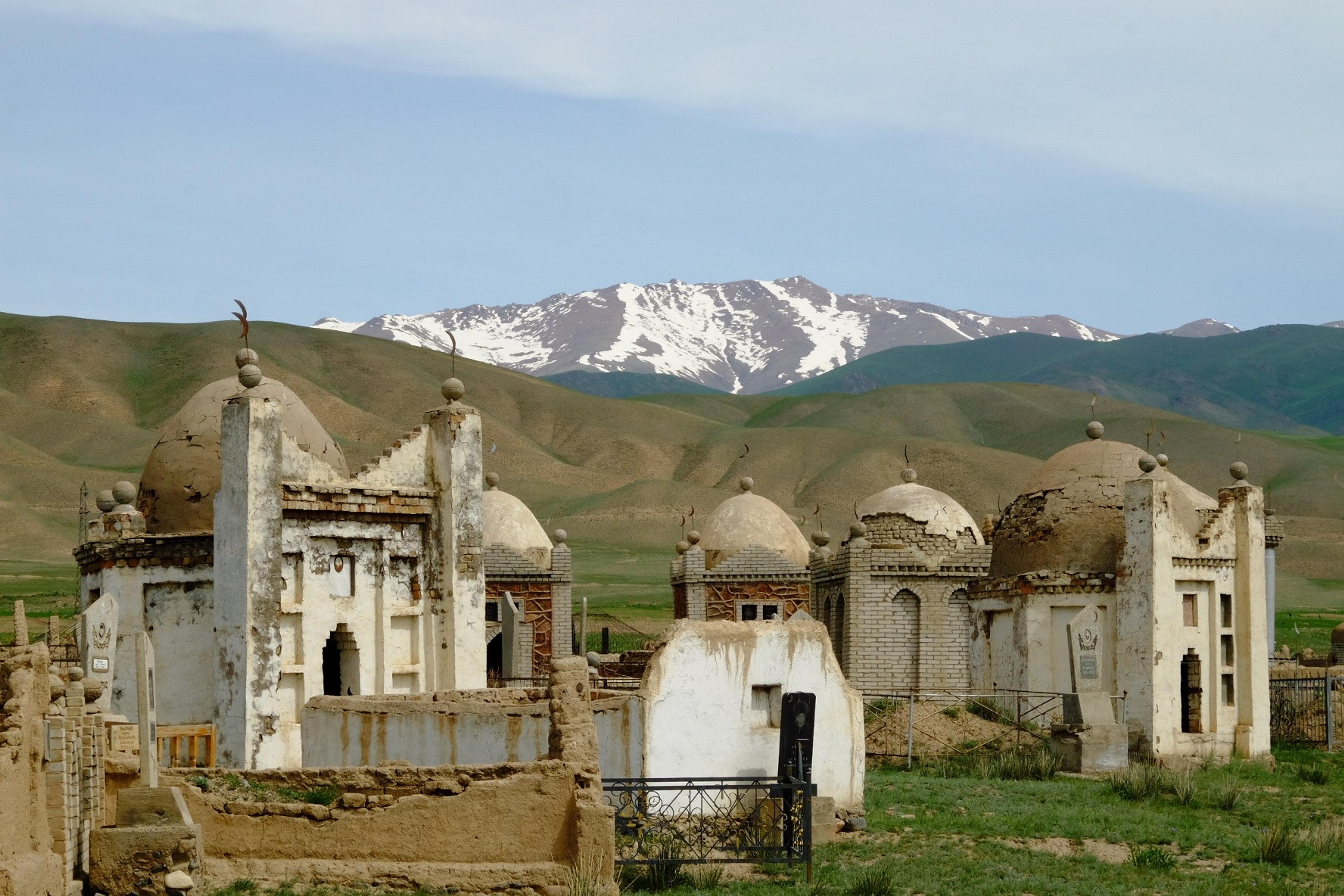 Historic mazars with domed structures stand against the backdrop of the snowy peaks of the Tien Shan mountains in Kyrgyzstan.