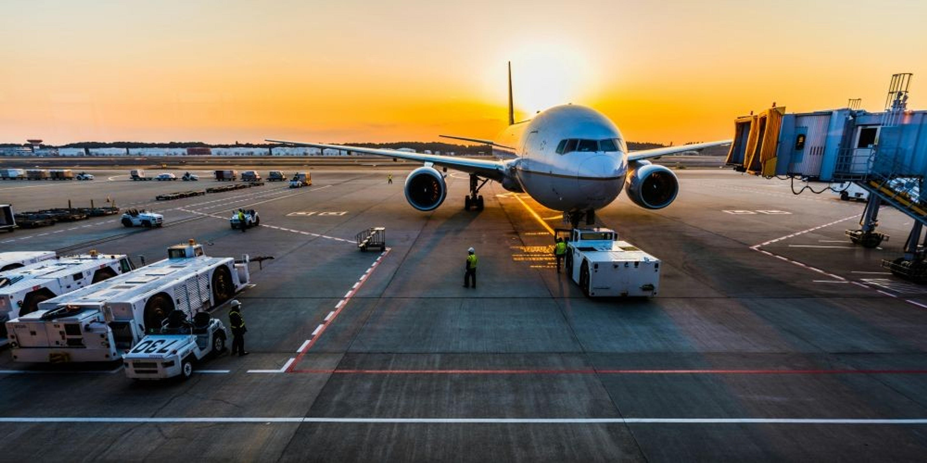 A large airplane is parked at Narita International Airport during a vibrant sunset, with ground crew and vehicles nearby.
